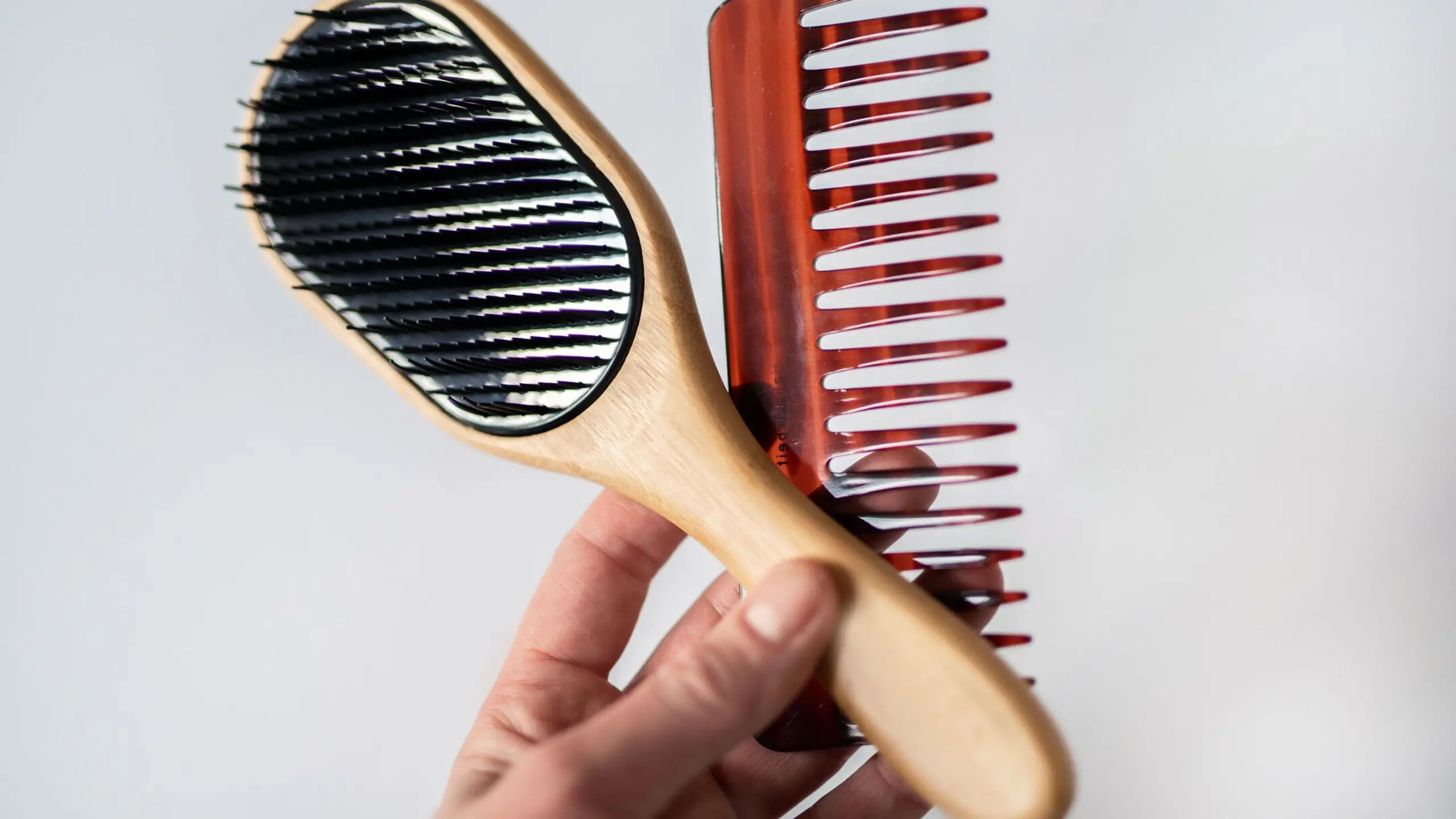 Frauenhand, die eine Haarbürste und einen Haarkamm hält