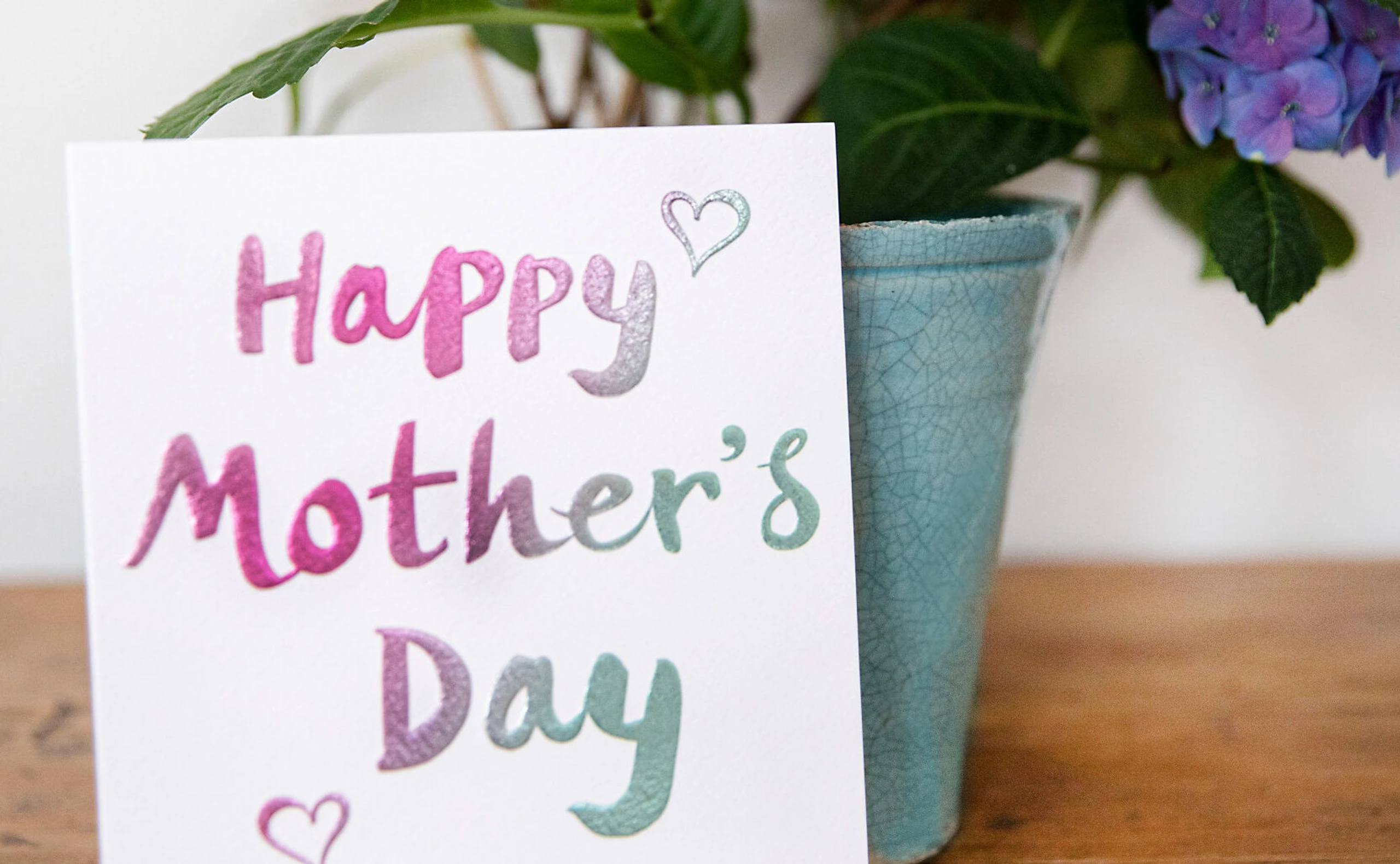 Muttertagskarte, die auf einem Tisch vor einem Blumenstrauß zu sehen ist