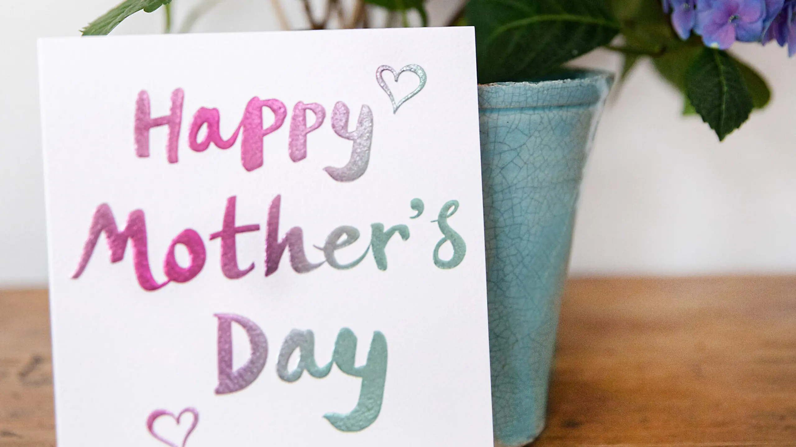 Muttertagskarte, die auf einem Tisch vor einem Blumenstrauß zu sehen ist