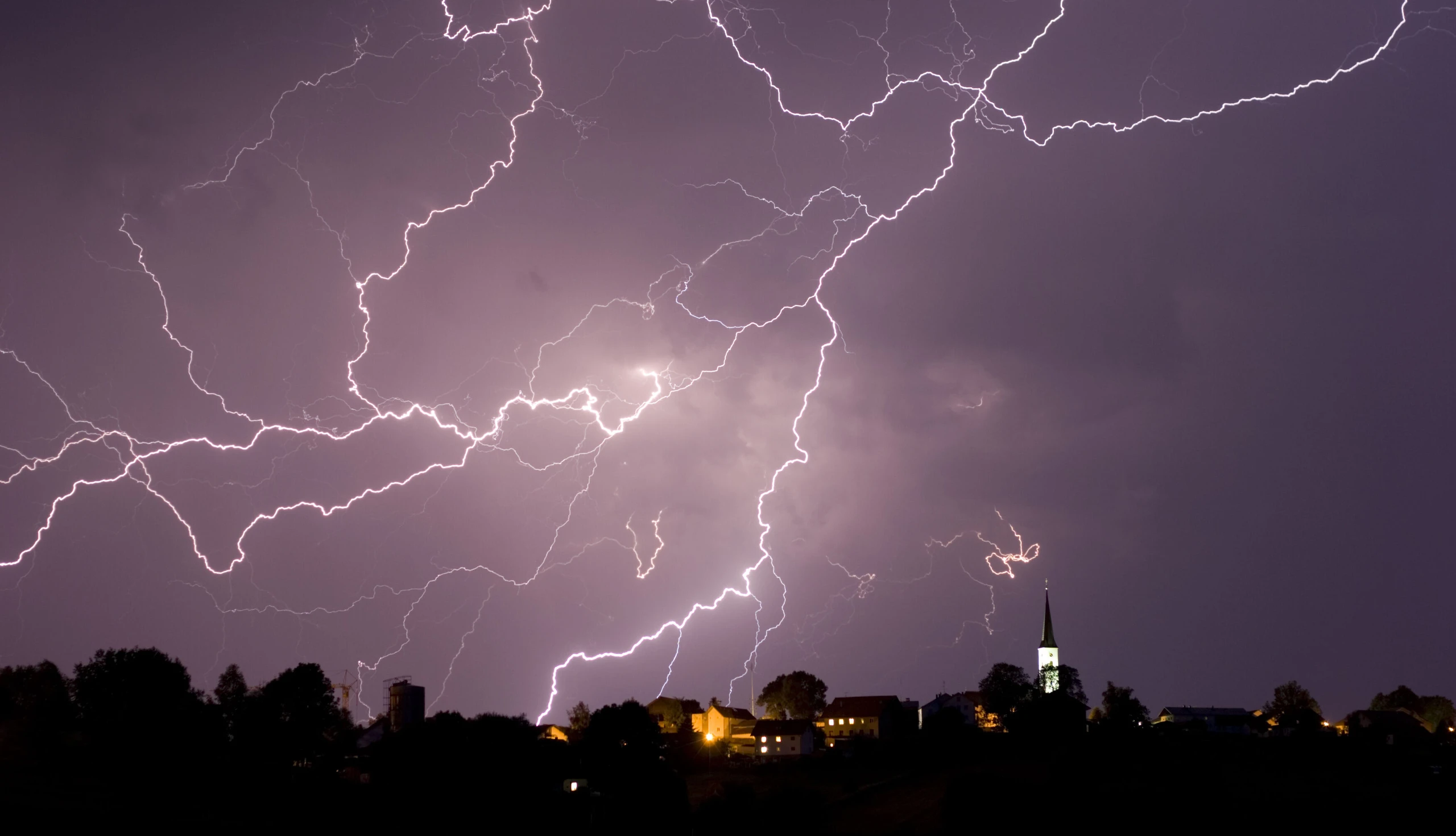 Blitze aus einer nächtlichen Gewitterwolke über einer Stadt