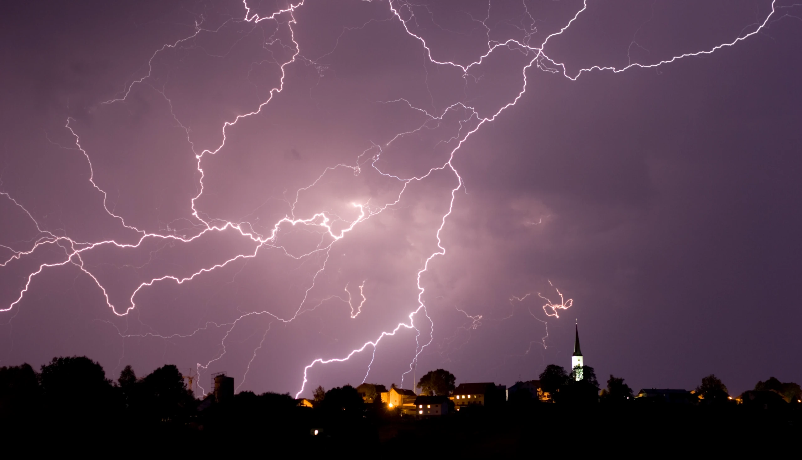 Blitze aus einer nächtlichen Gewitterwolke über einer Stadt