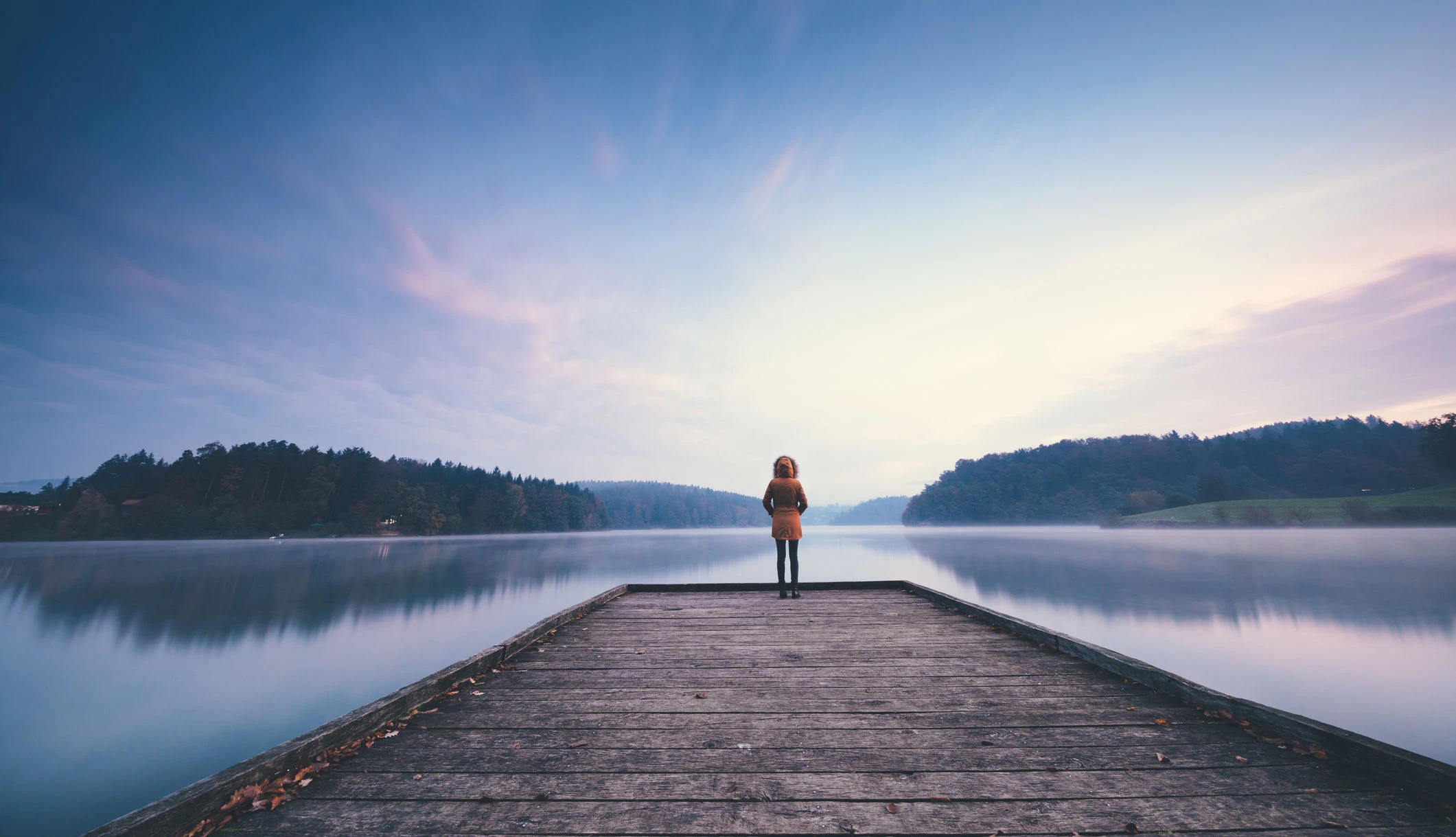 Eine Person steht einsam auf einem Steg am See.
