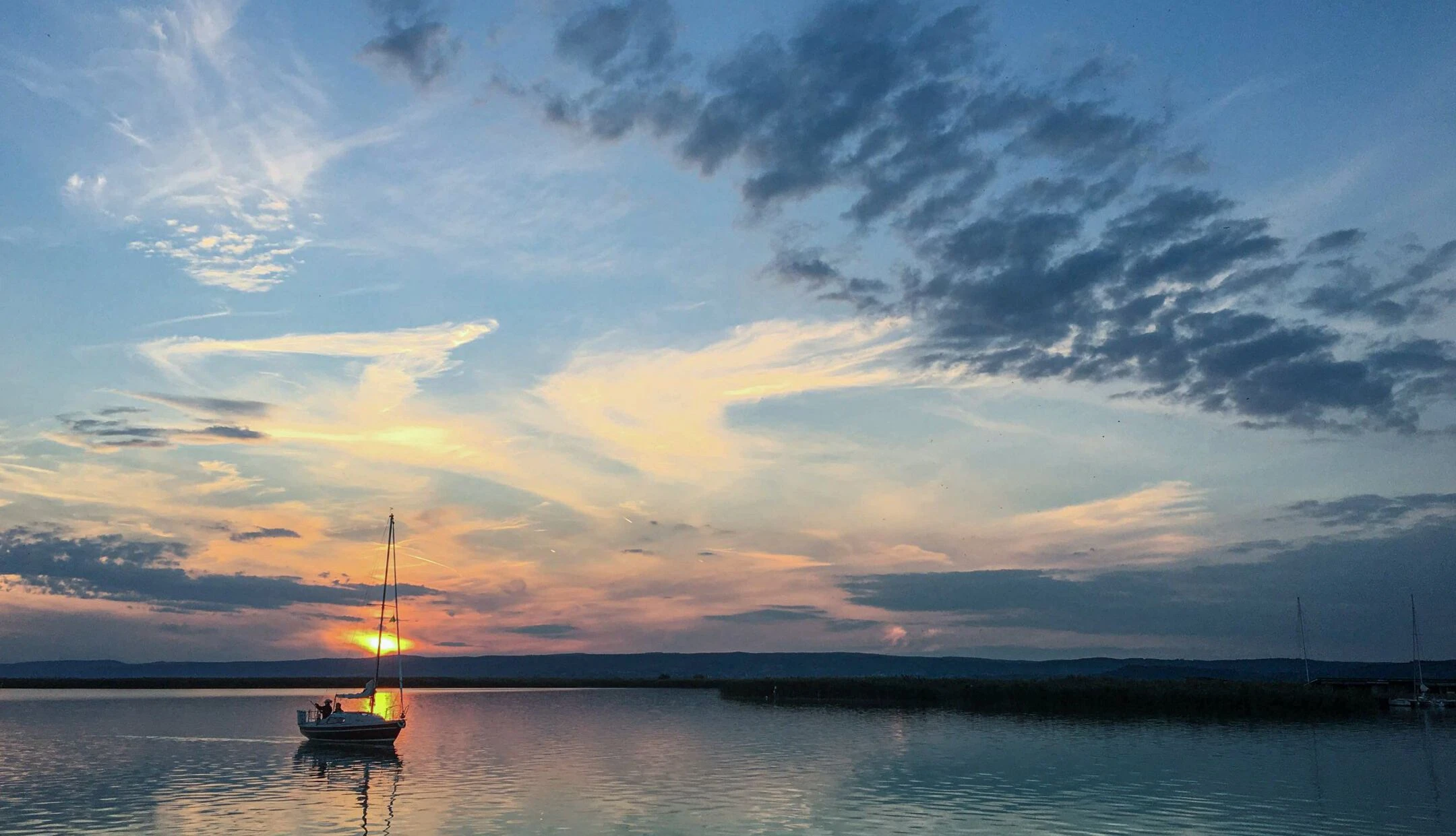 Ein Segelboot ist bei Sonnenuntergang am Neusiedler See unterwegs.