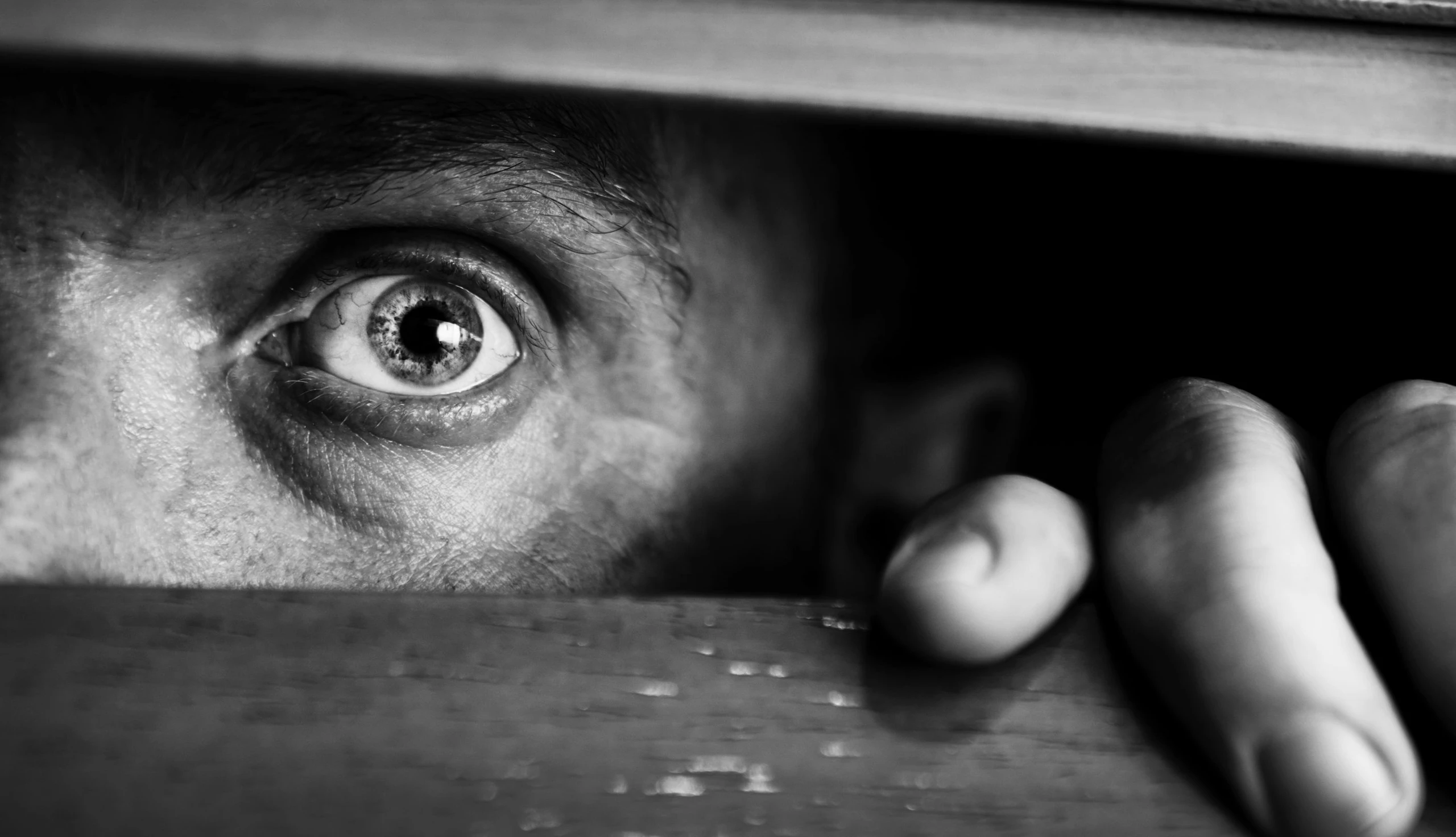 Mann mit vor Angst geweiteten Augen schaut durch Schlitz