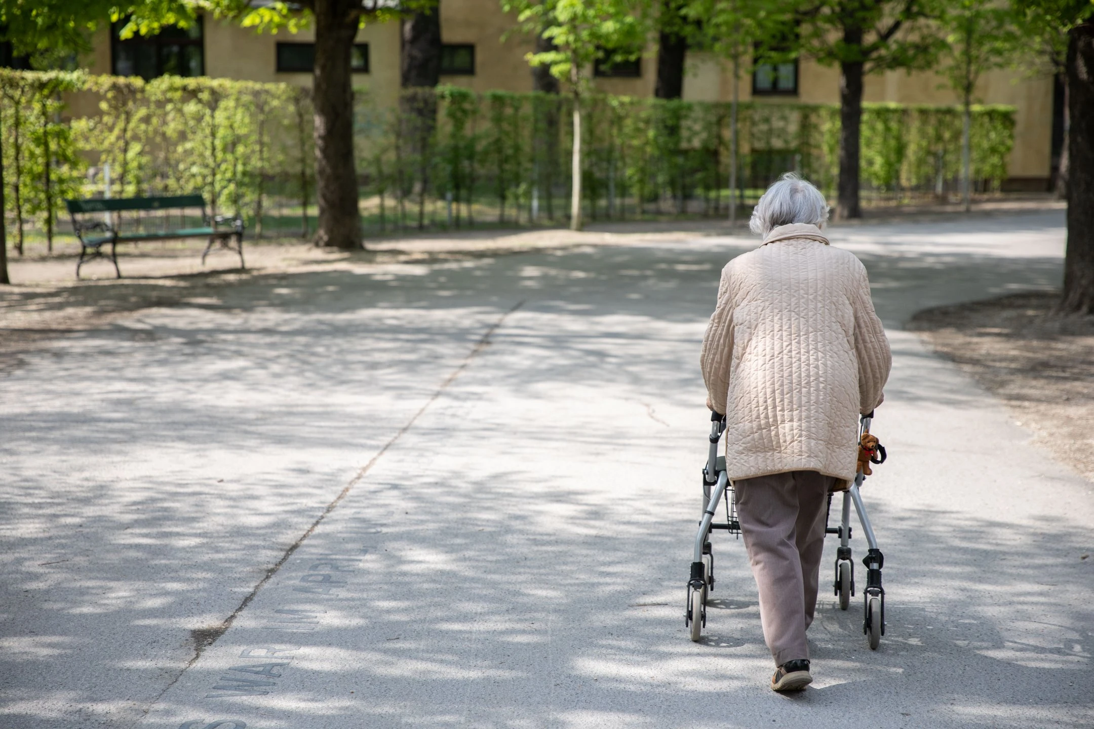 Eine Pensionistin geht im Park mit einem Rollator spazieren.