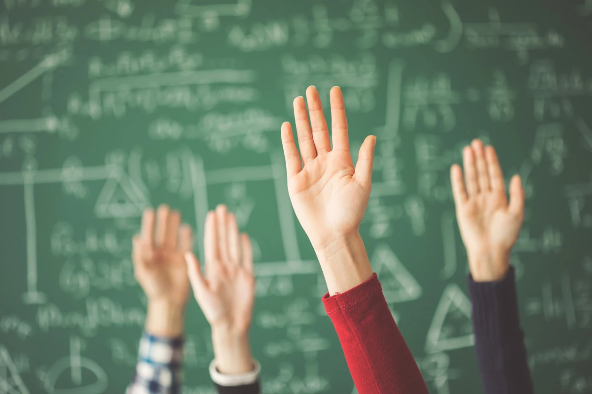 Schüler:innen zeigen in der Schule auf.