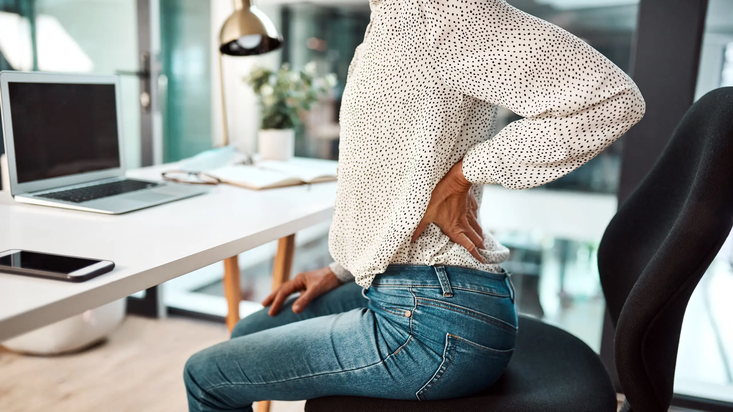 Sitzende Frau, die mit einer Hand ihren schmerzenden Rücken hält