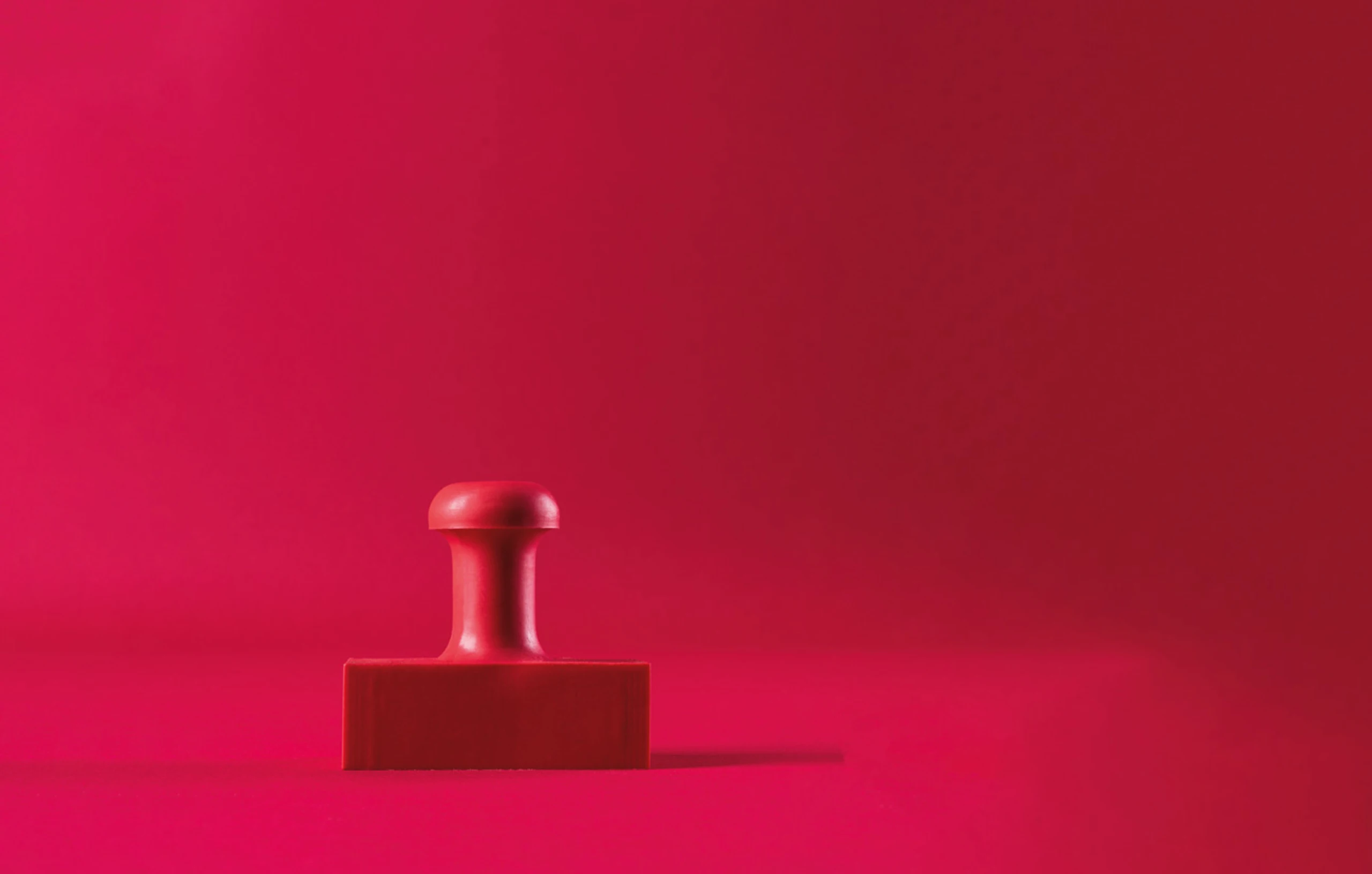 Symbolbild für Bürokratie: Ein Stempel steht vor einem rot-pinkem Hintergrund.