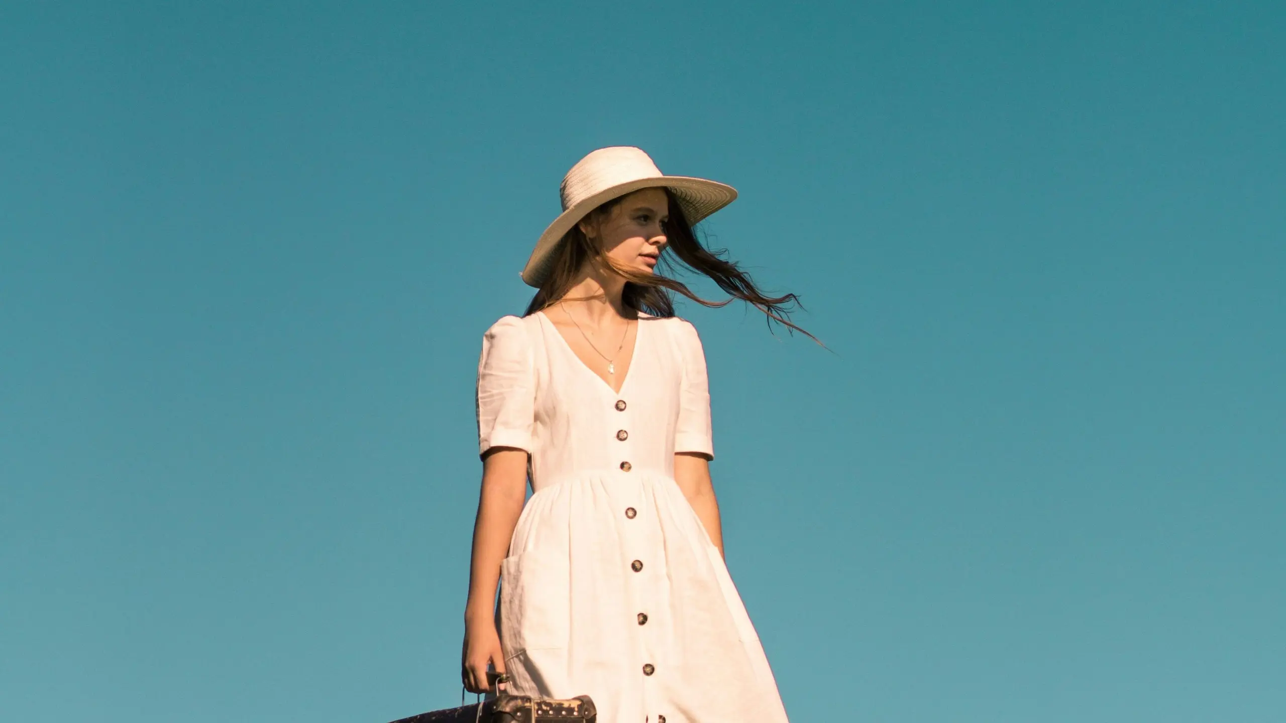Frau steht mit Koffer in der Hand auf Wiese