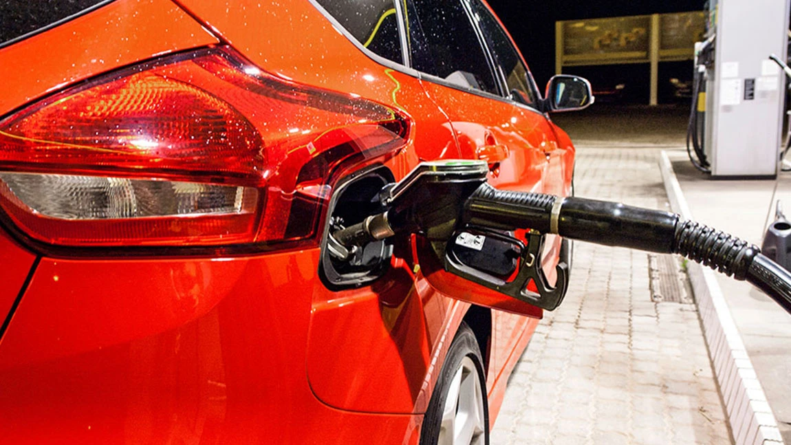 Ein rotes Auto steht an einer Tankstelle mit dem Zapfhahn im Tank.