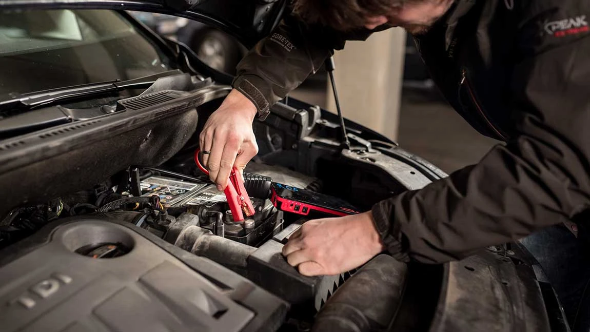 Anschließen eines Starterkabels im Motorraum eines Autos um Starthilfe geben zu können.