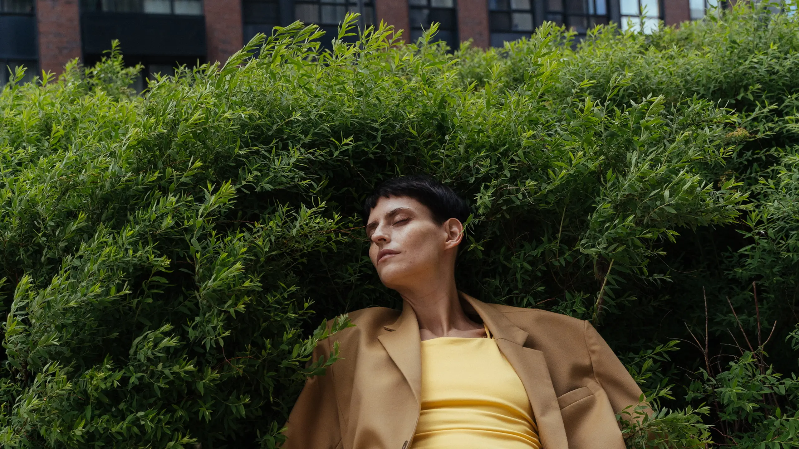 Frau mit geschlossenen Augen, angelehnt an ein Gebüsch