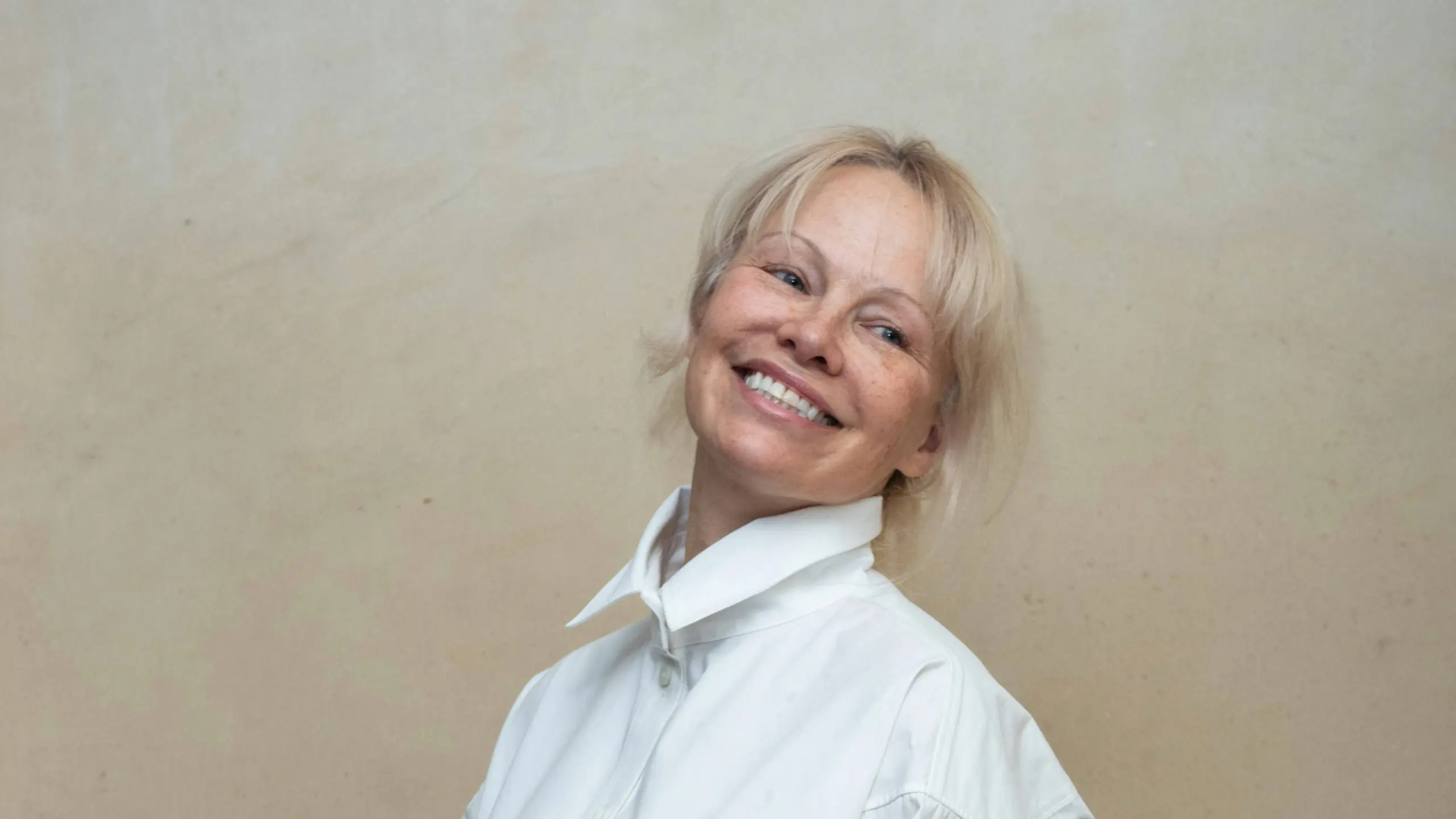 Pamela Anderson im weißen Outfit und schwarzer Tasche