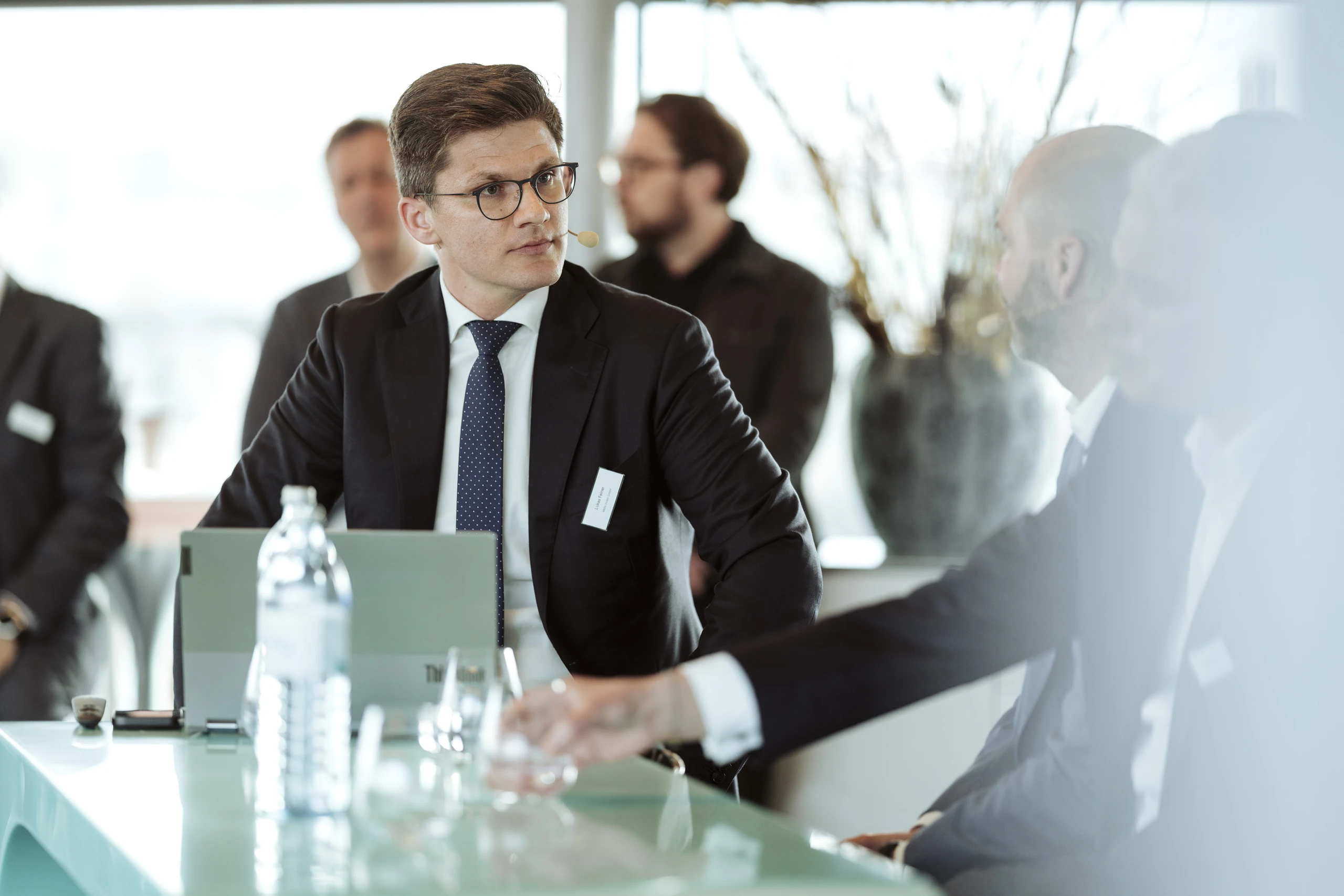 Mann im Anzug bei einem Business-Meeting.  Konzentrierter Blick, Laptop und Wasserflasche auf dem Tisch.