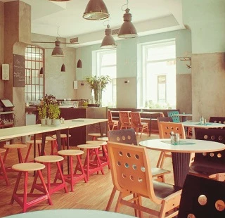 Modernes Café mit hellem Holzmobiliar, Pastellwänden & industriellen Lampen. Freundliches Ambiente.
