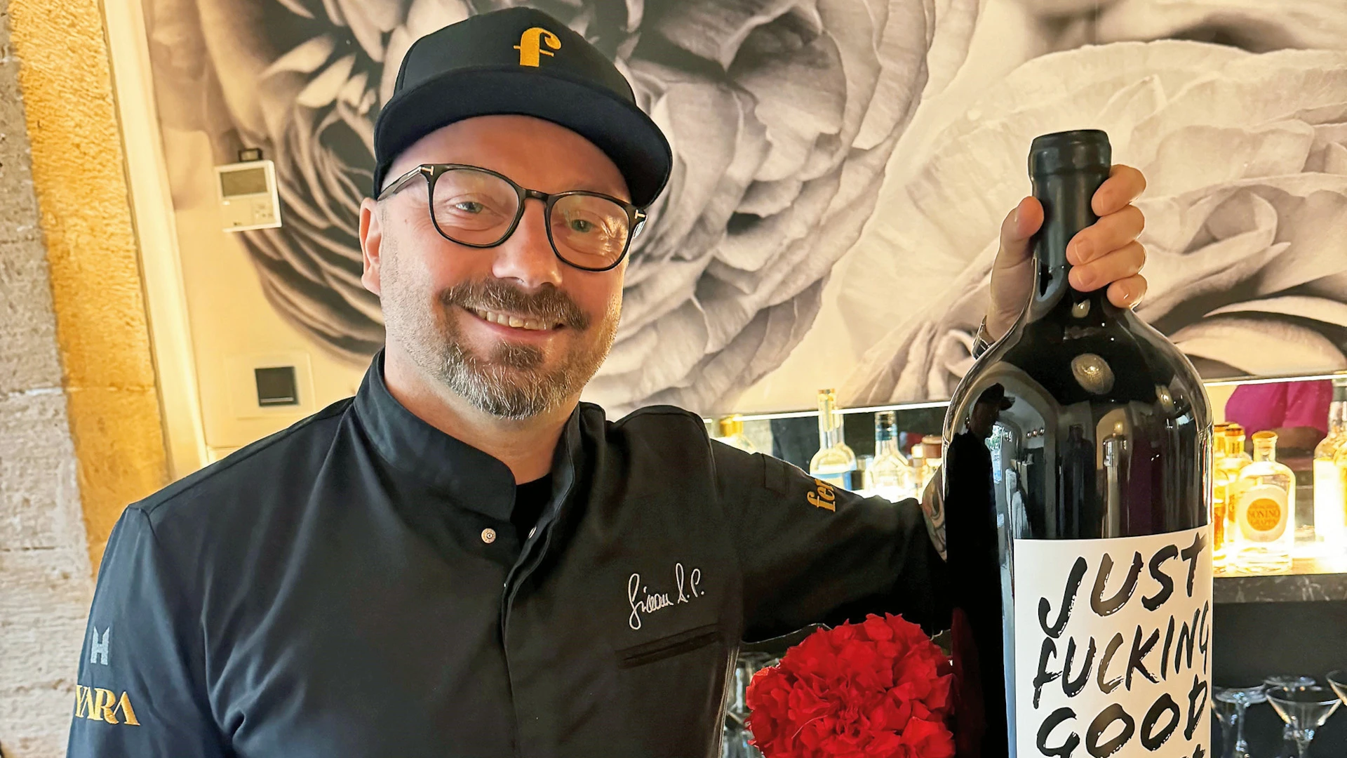 Haubenkoch Simon Petutschnig hält eine große Weinflasche, auf der "Just fucking good wine" steht.