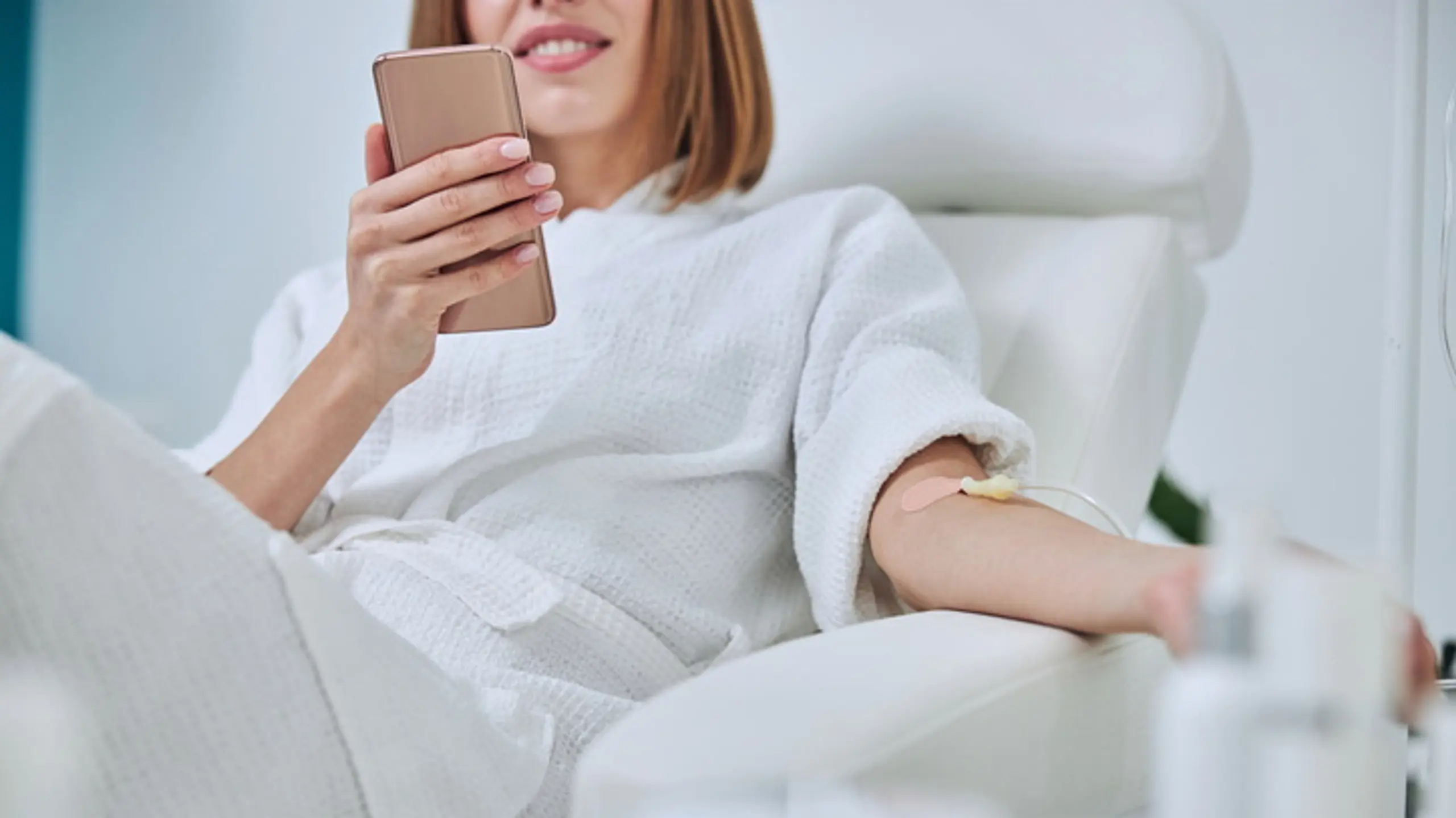Frau mit Handy hängt an einer Infusion