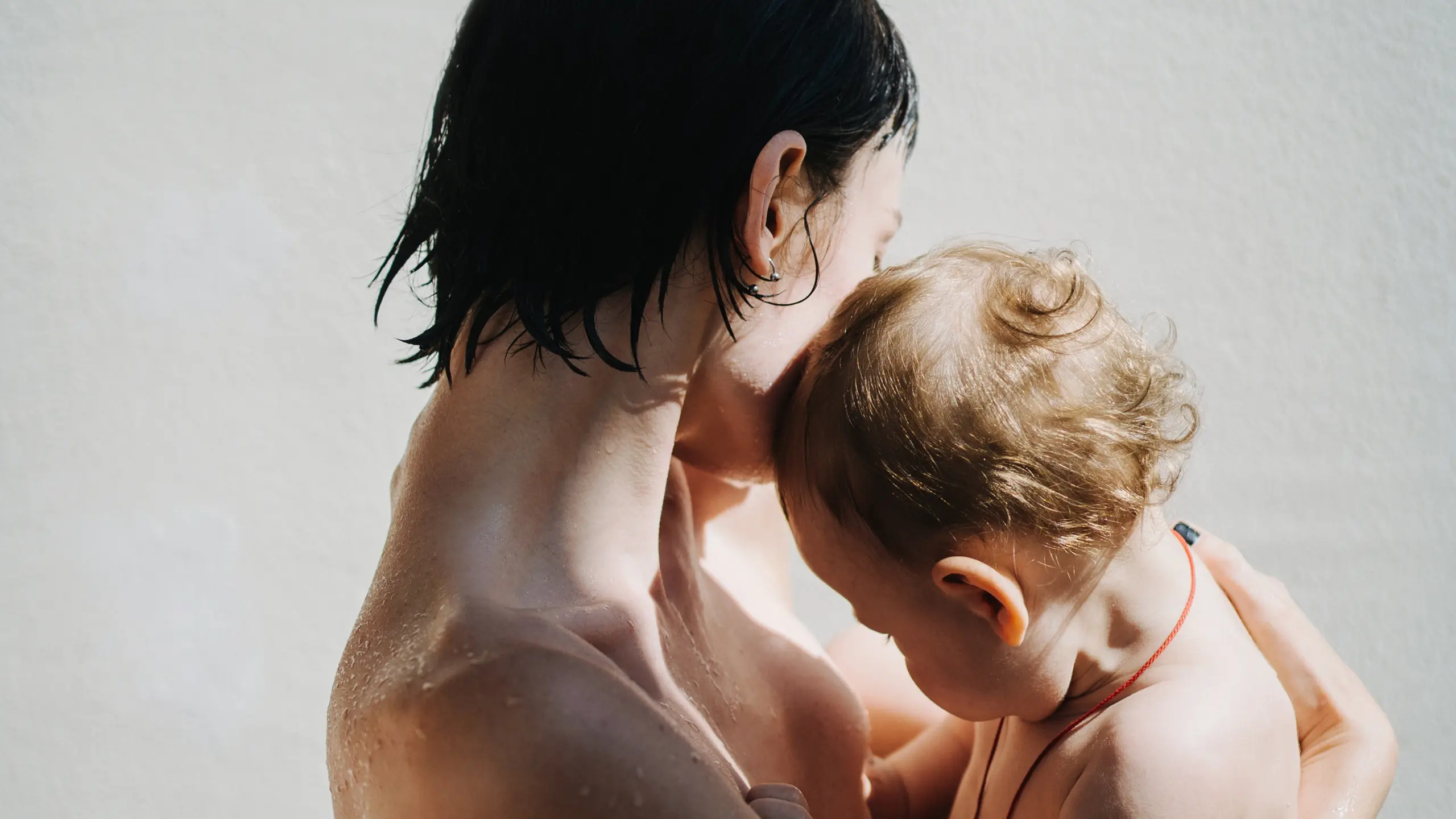 Eine nackte Frau hält ein nacktes Baby auf dem Arm, beide Gesichter schauen von der Kamera weg