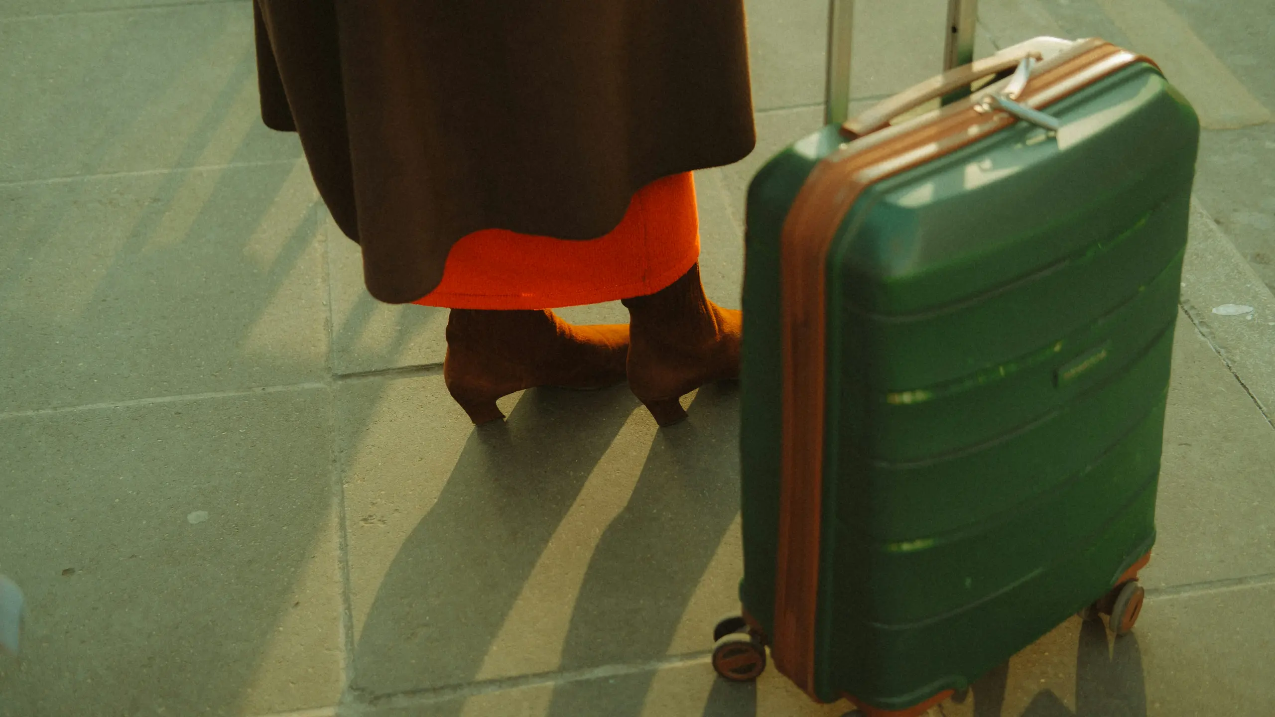 ein Grüner Koffer neben den Beinen einer Frau