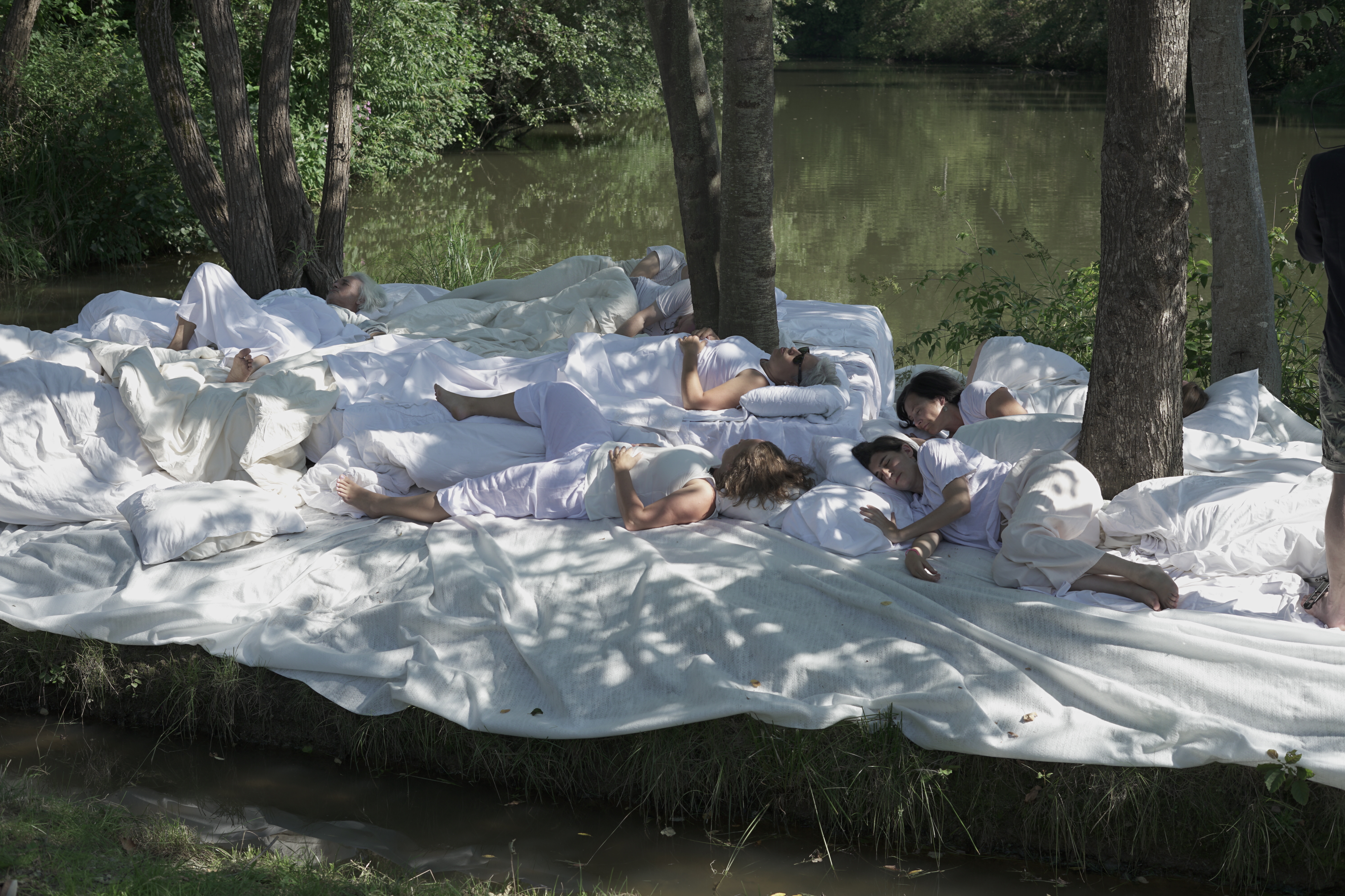 Szene an einem Fluss, Menschen liegen auf weißen Tüchern und Pölstern