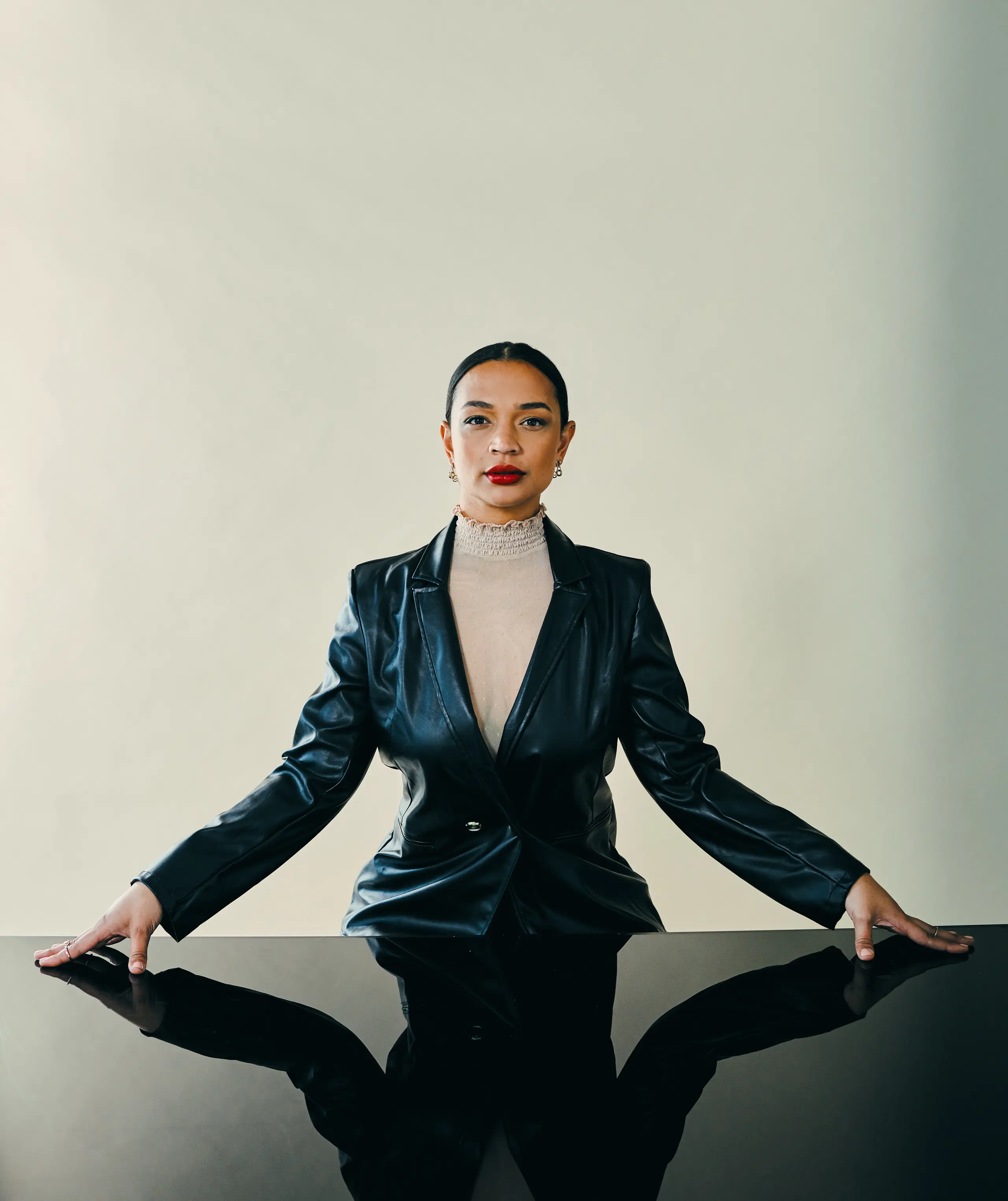 Frau mit rotem Lippenstift steht in selbstbewusster Pose vor einem Tisch