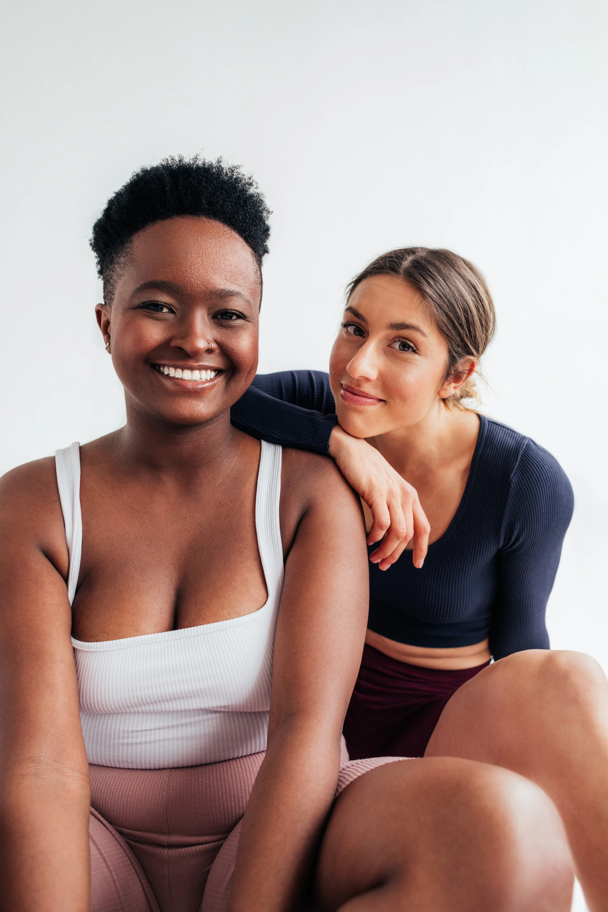 Zwei lächelnde Frauen, eine ist Schwarz und hat kurze haare, die andere ist weiß und hat längere Haare und einen Zopf