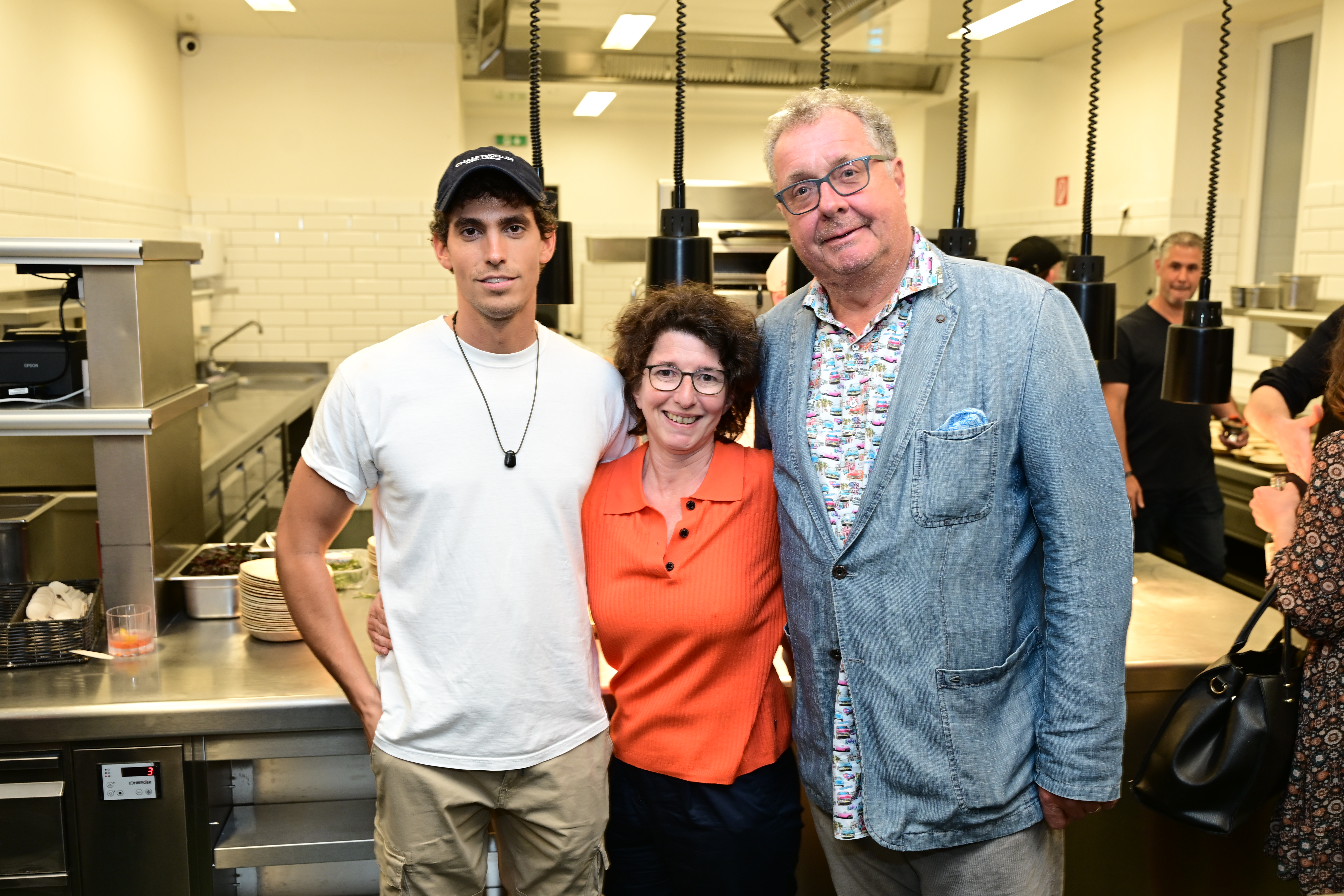 Gruppenfoto in Restaurantküche: Junger Mann, Frau in Orange, älterer Mann in Jeansjacke. Nikon Z6_3.