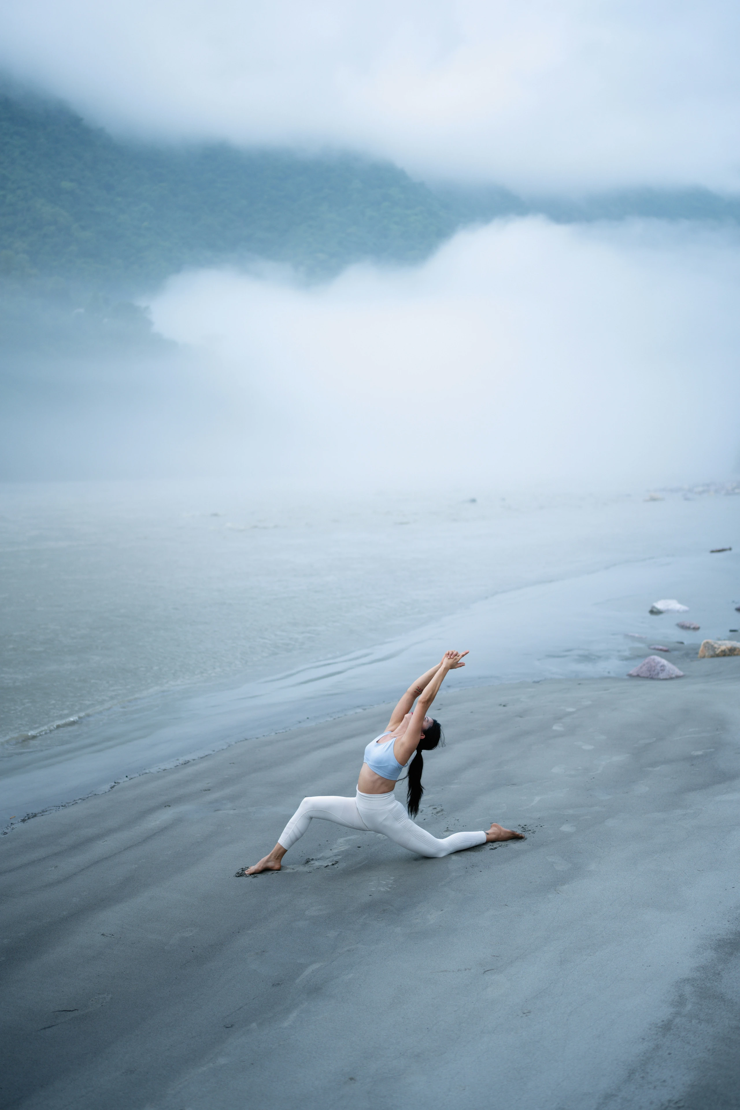 Eine Frau macht Yoga am Strand, es etwas nebelig oder wolkig
