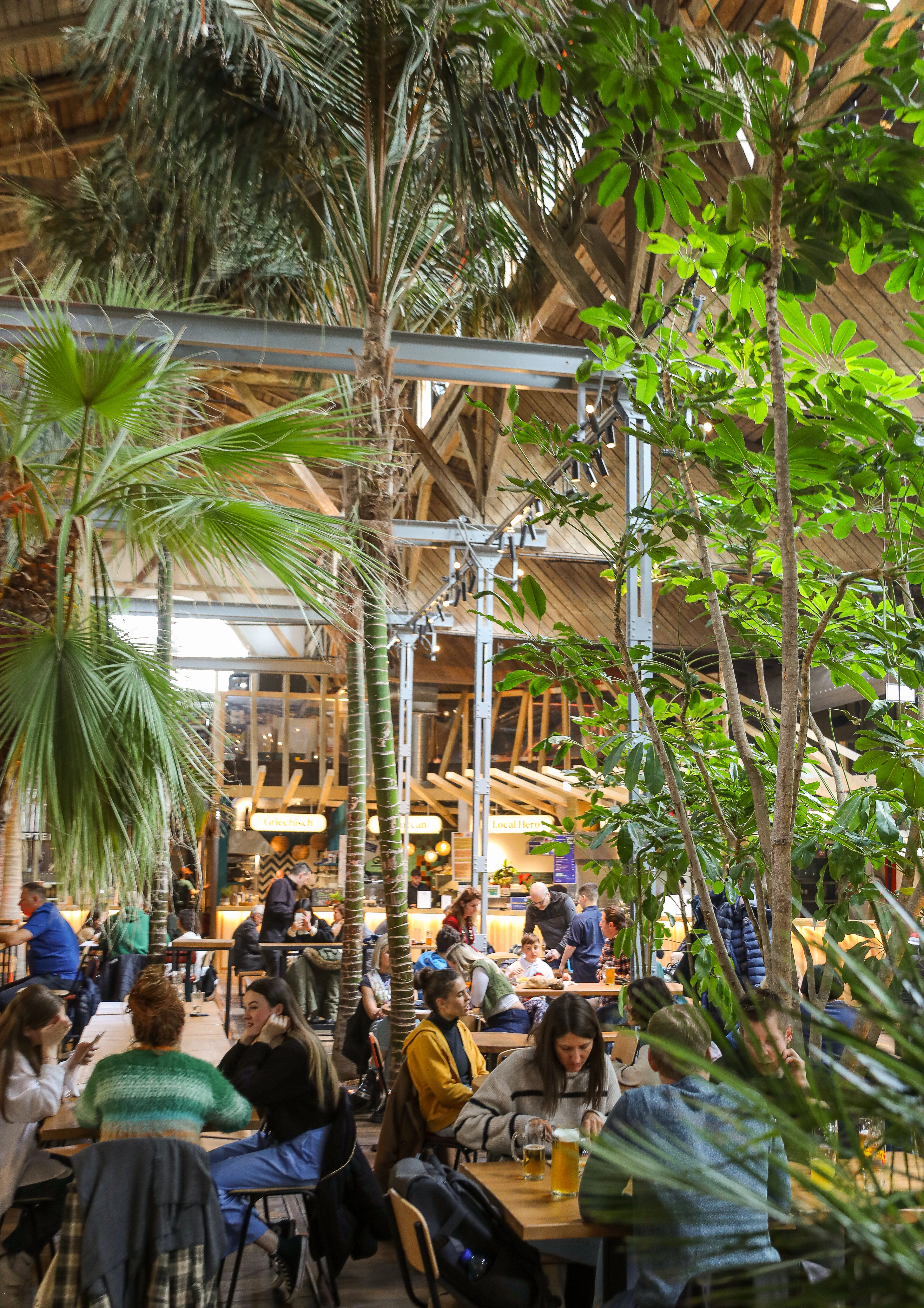 Entspannte Markthalle mit üppigem Grün, Menschen beim Essen und Trinken.