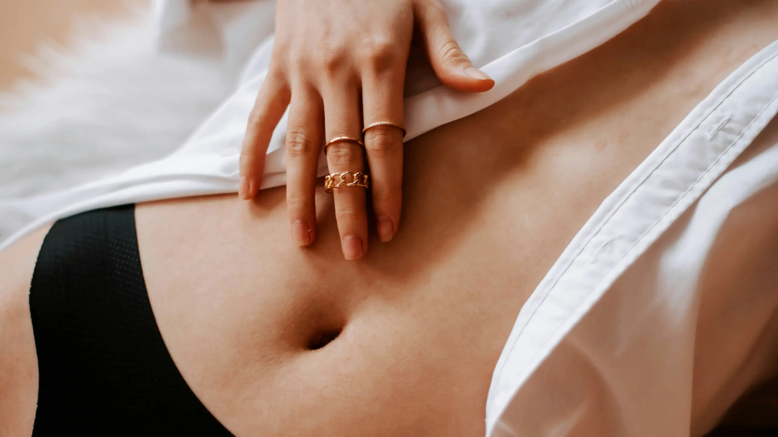 Der Oberkörper einer Frau, sie liegt auf einem Teppich, hat ein offenes Hemd an und ihre Hand auf den nackten Bauch gelegt