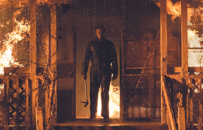 Killer Michael Myers kommt aus der Eingangstüre eines brennenden Gebäudes mit einer Hacke bewaffnet