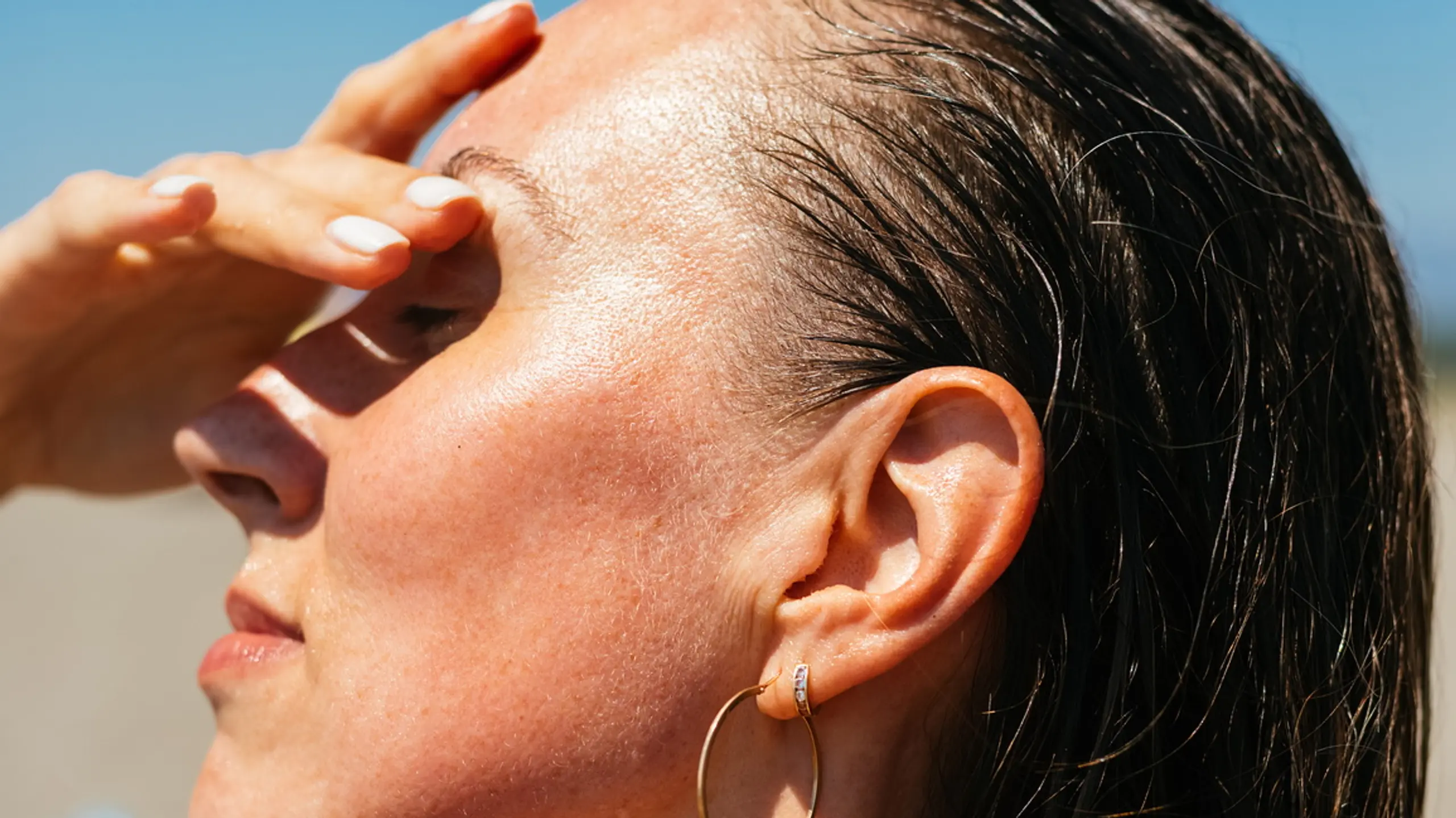 Frau mit nassen Haaren steht Richtung Sonne und bedeckt Augen