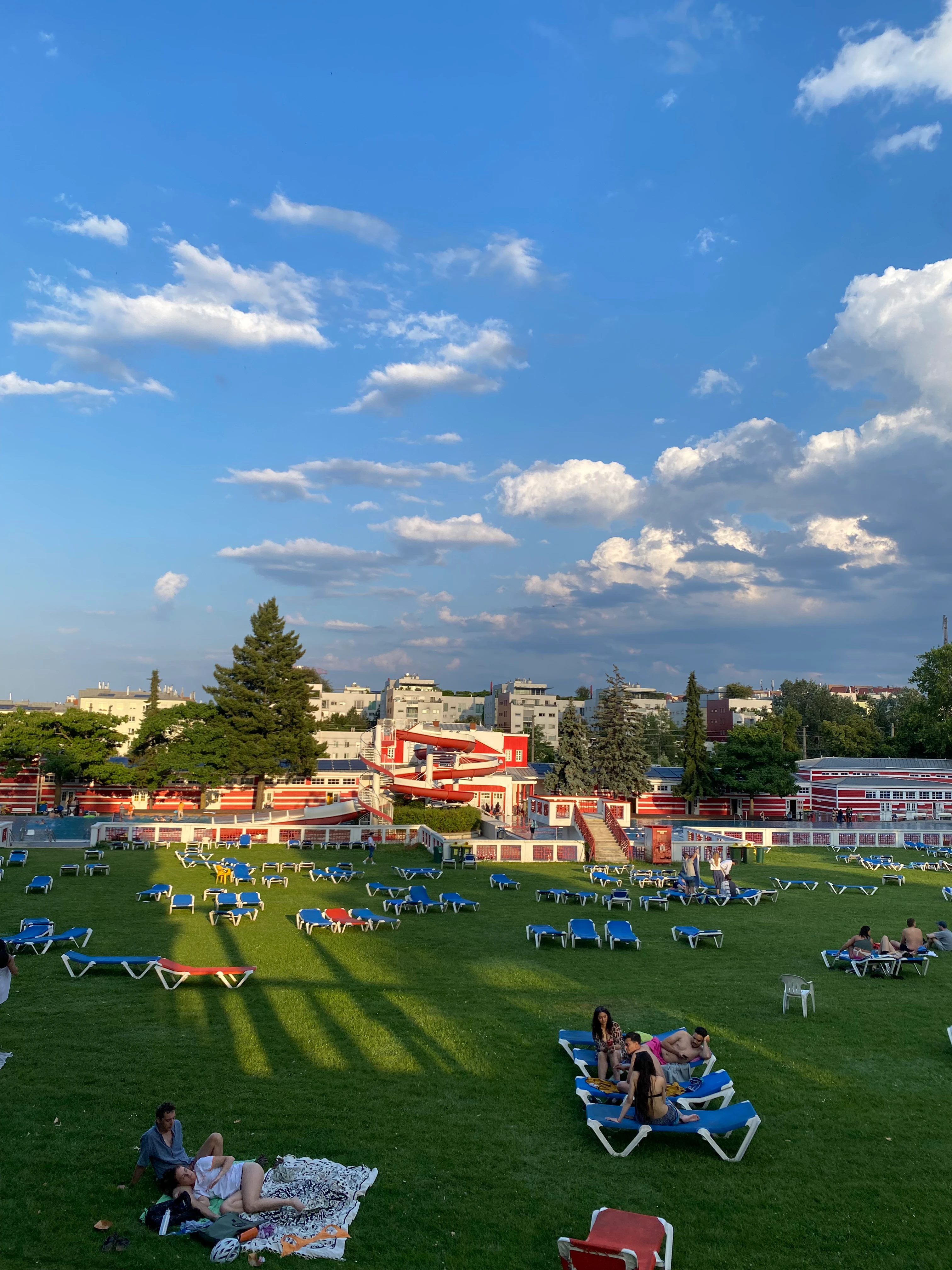 Sonniger Tag im Freibad: Entspannte Menschen auf Liegestühlen, Wasserrutschen im Hintergrund.