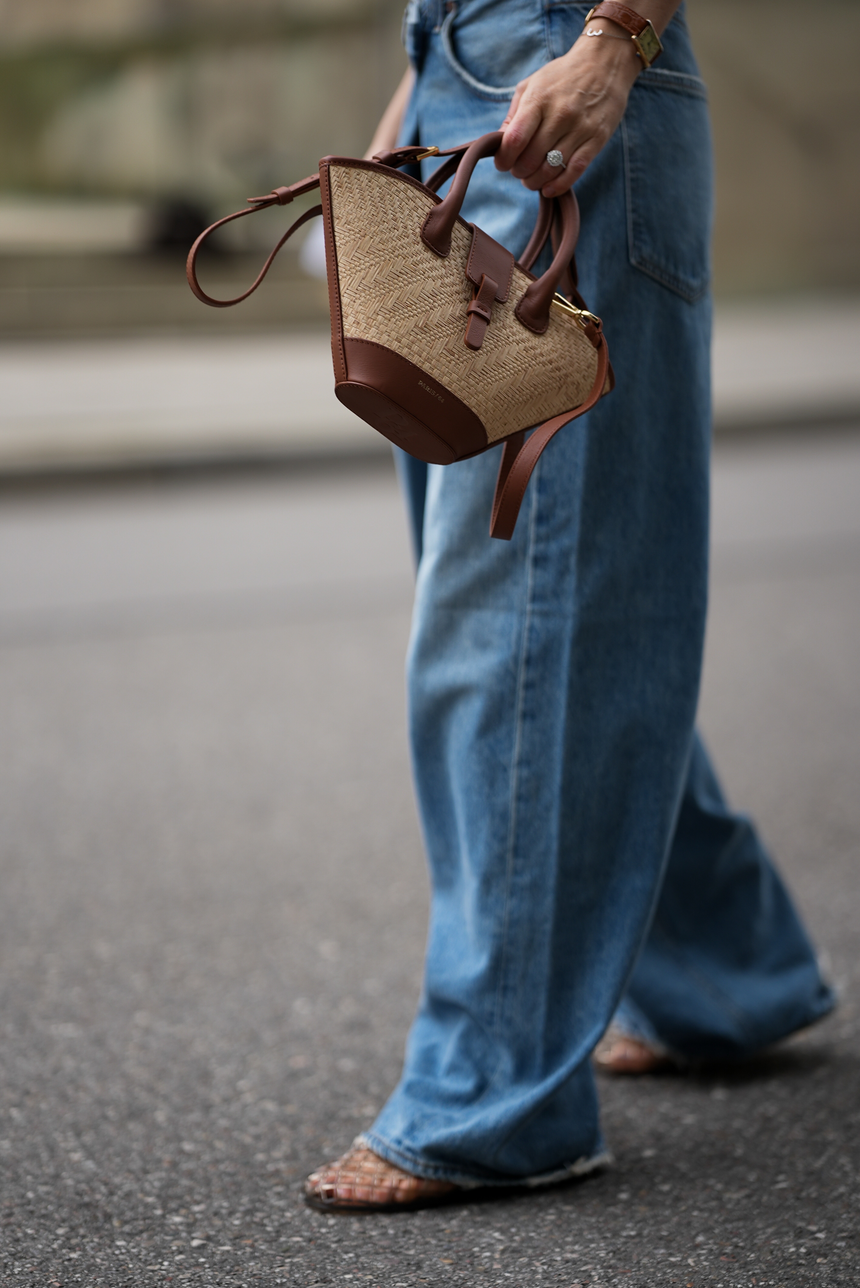 Eine Frau von der Hüfte abwärts. Sie trägt eine blaue Jeans und hält eine Tasche aus Bast in der Hand