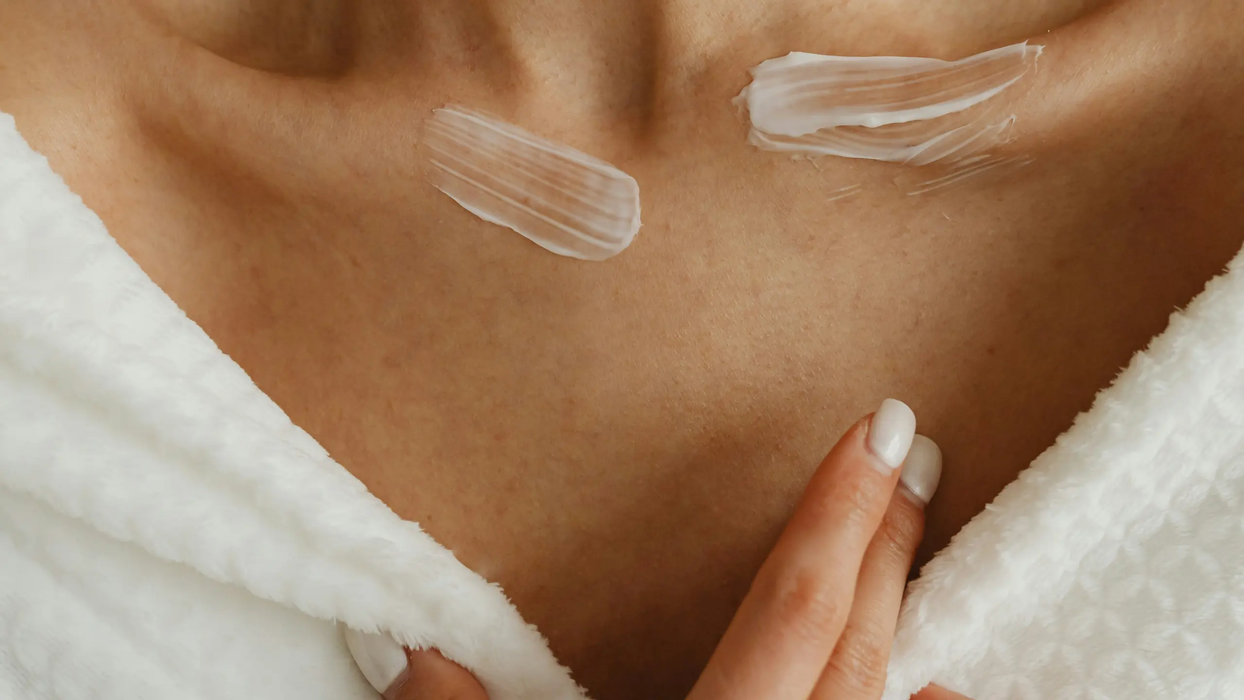 Frau in Bademantel mit Creme-Swatches auf den Schlüsselbeinen