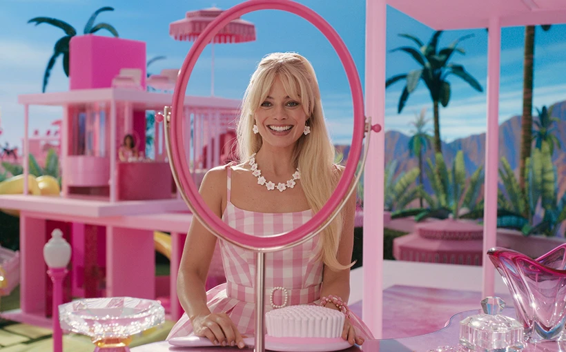 Margot Robbie schaut als Barbie in einen Spiegel, rundherum ist alles rosa