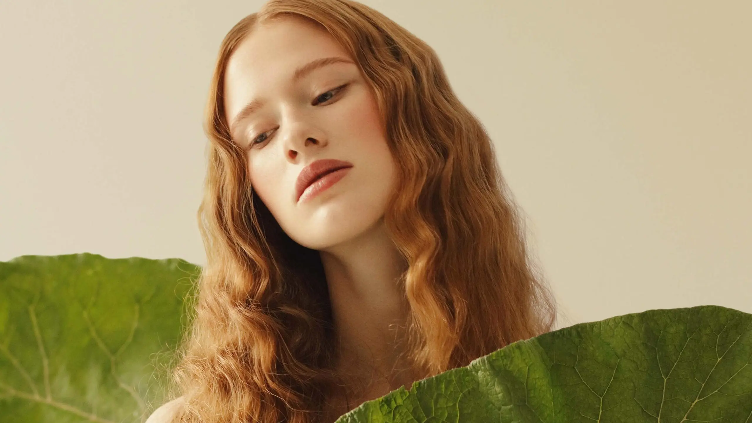 Natürliches Model vor beigem Hintergrund und mit großen grünen Blättern und