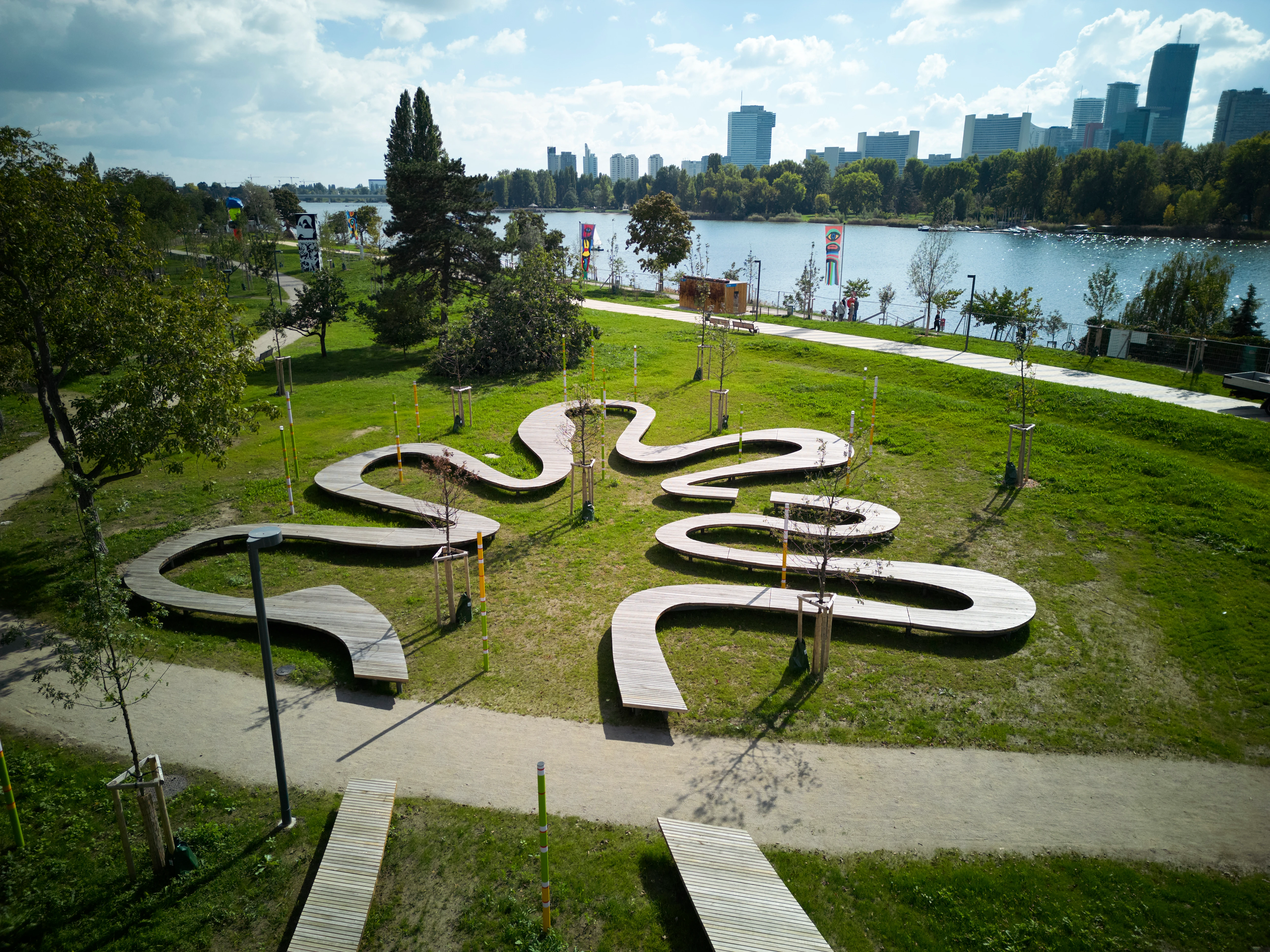 Parkansicht in Wien mit geschwungenen Holzbänken und See im Hintergrund.