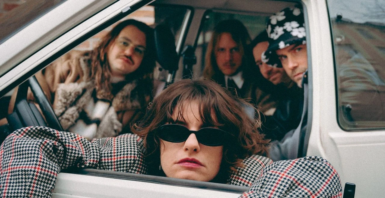 Gruppe von Personen in einem weißen Lieferwagen, Frau mit Sonnenbrille lehnt aus dem Fenster