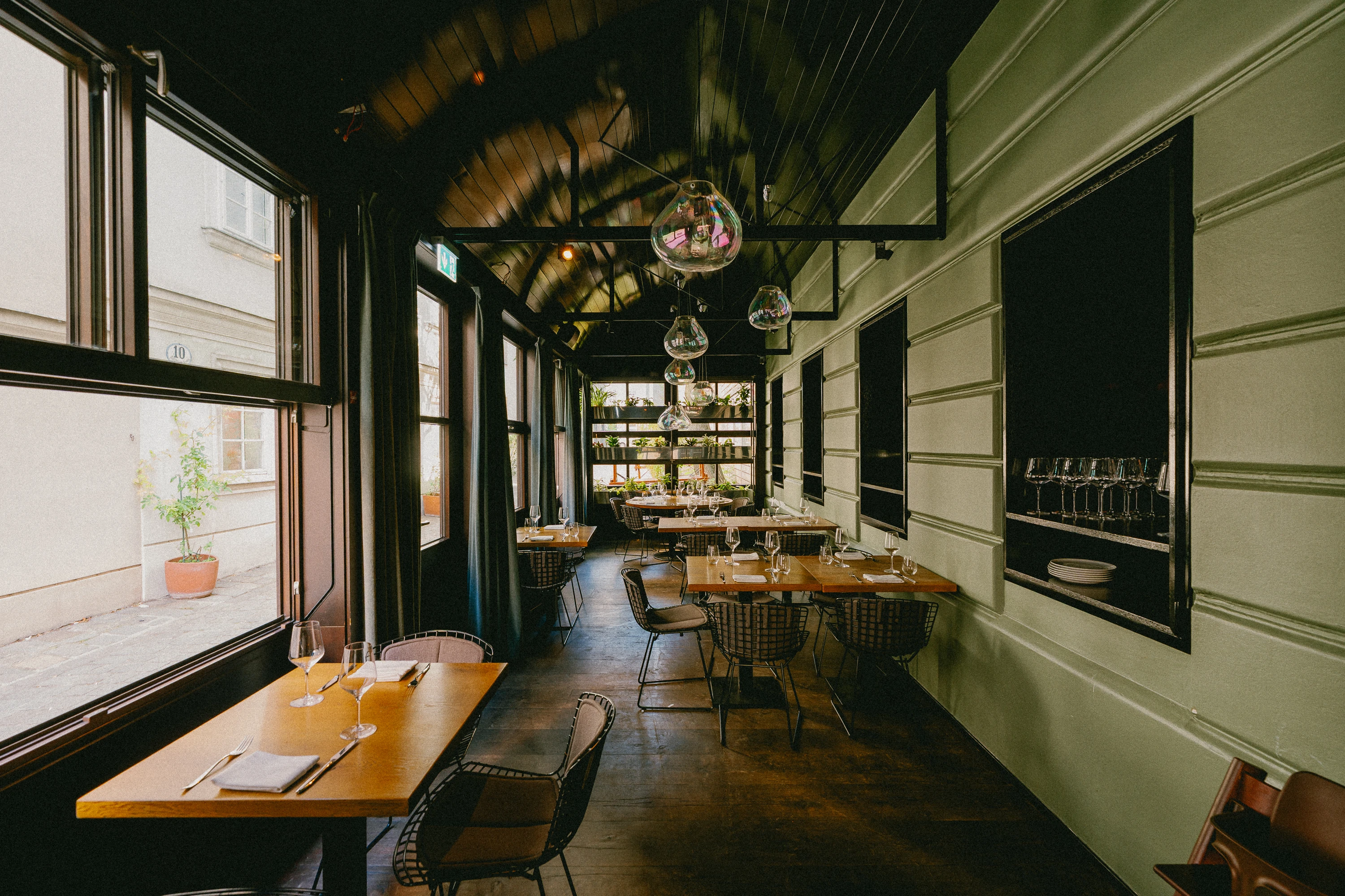 Elegantes Restaurant-Interieur mit Holztischen, Metallstühlen und Glasleuchten.