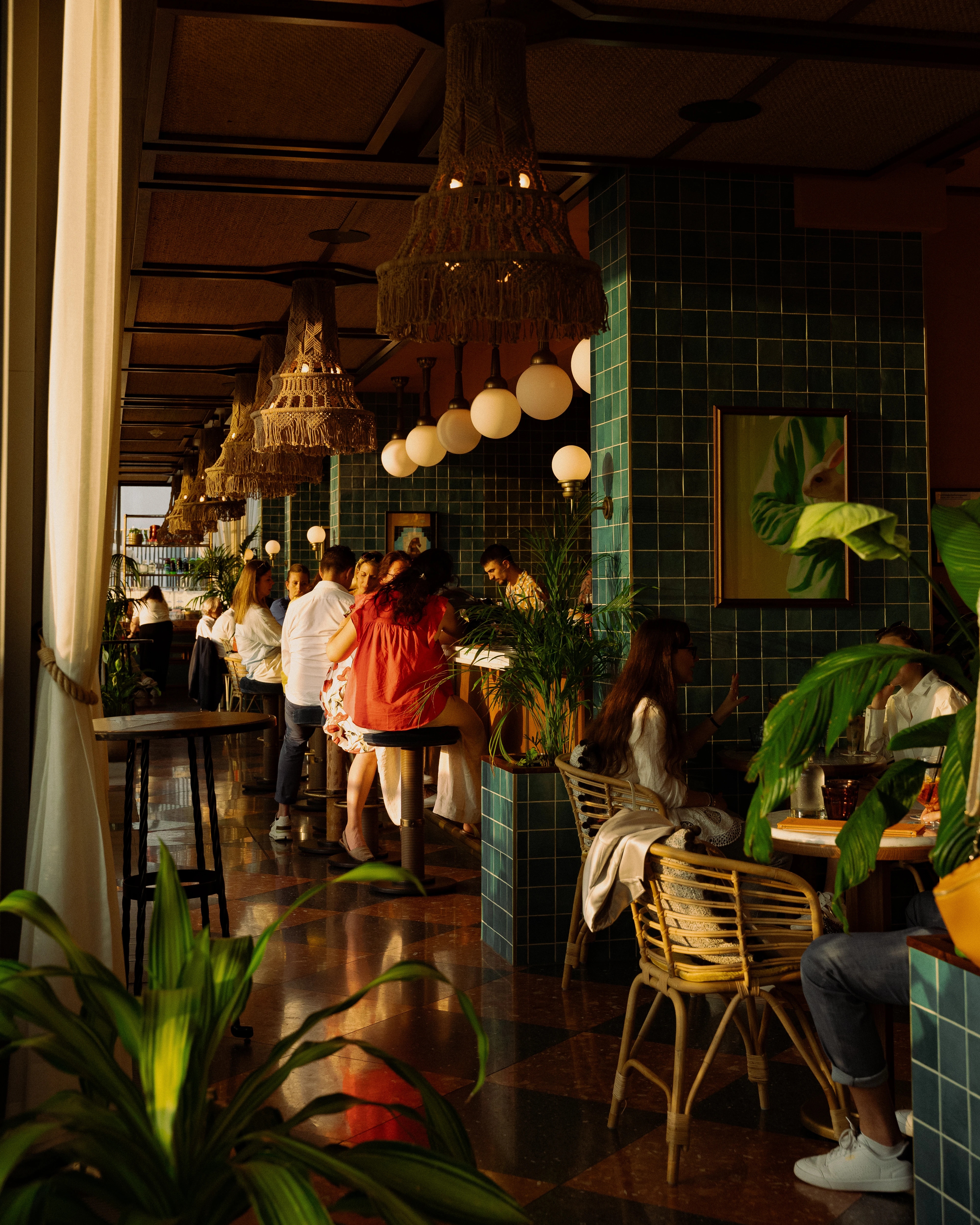 Elegantes Restaurant mit Gästen, Pflanzen und dekorativen Lampen im Innenraum.
