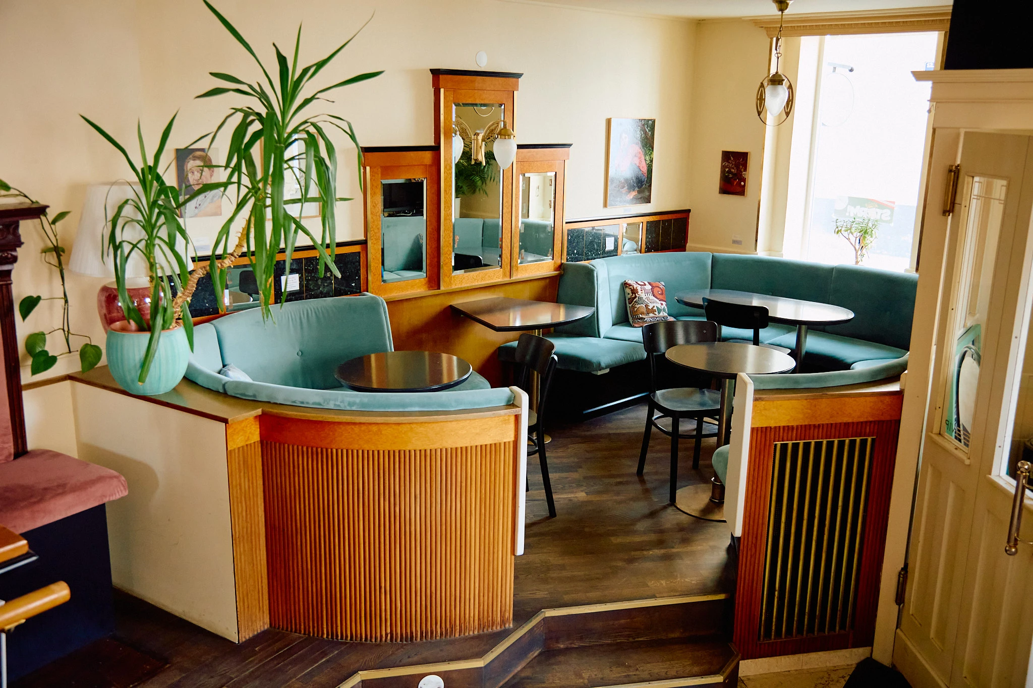 © Michael Lukele Innenansicht eines stilvollen Cafés oder Restaurants mit türkisfarbenen Polsterbänken, Holzelementen und einladender Atmosphäre.