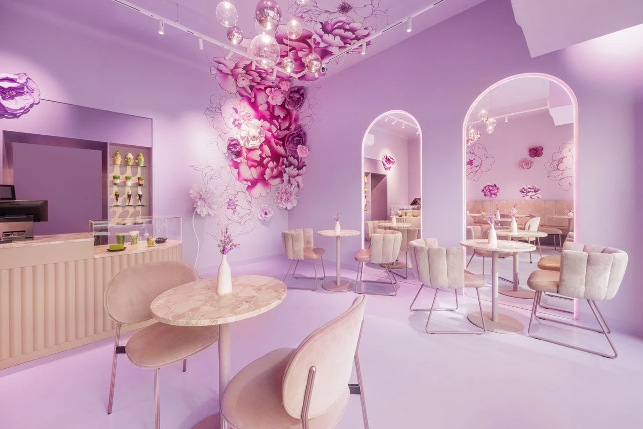 Elegantes Café-Interieur in Lila- und Rosatönen mit floralen Akzenten und Marmortischen.