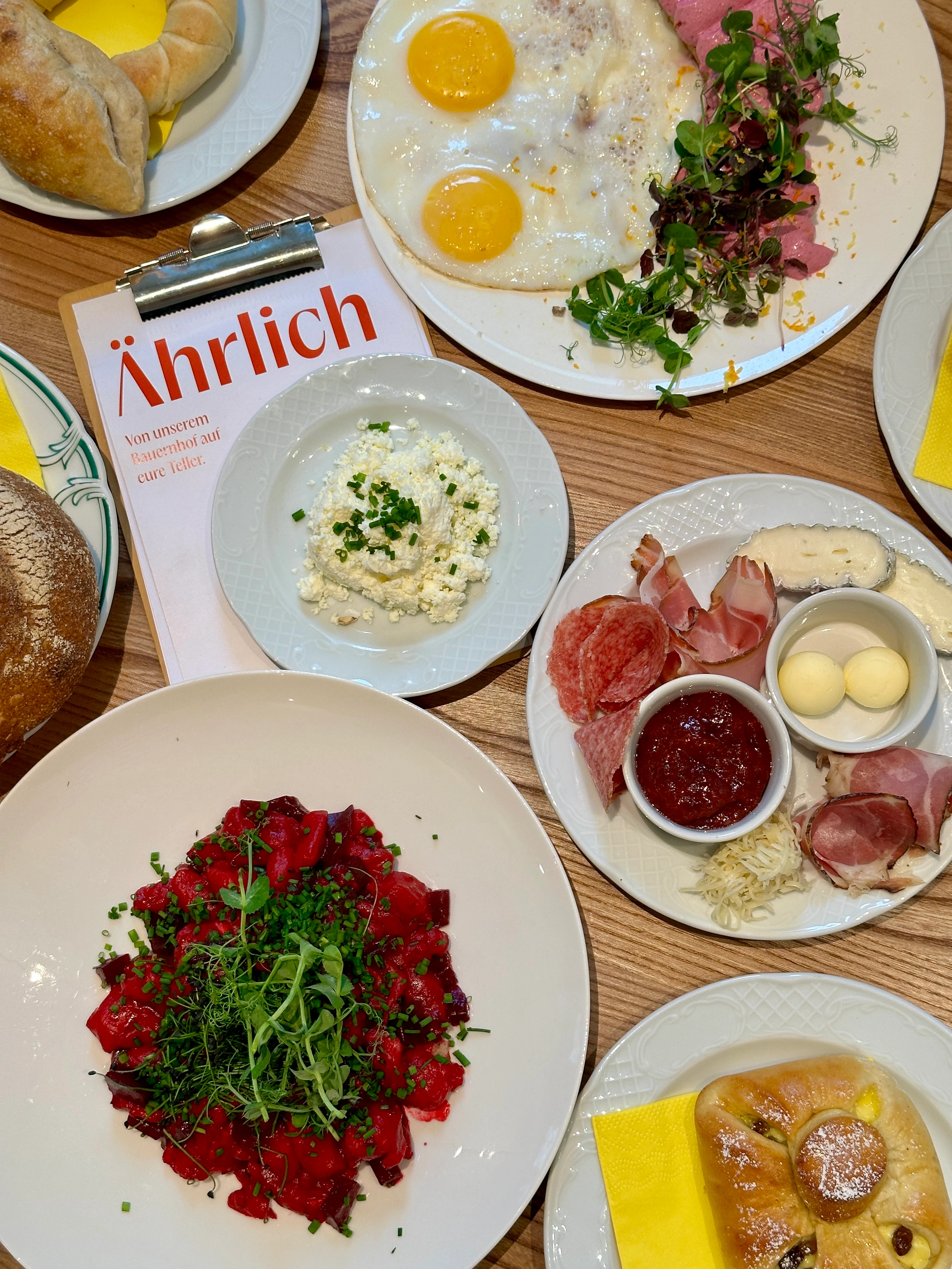 Vielfalt an Speisen auf einem Tisch, darunter Bauernfrühstück, Käseplatte, Brot und süßes Gebäck.