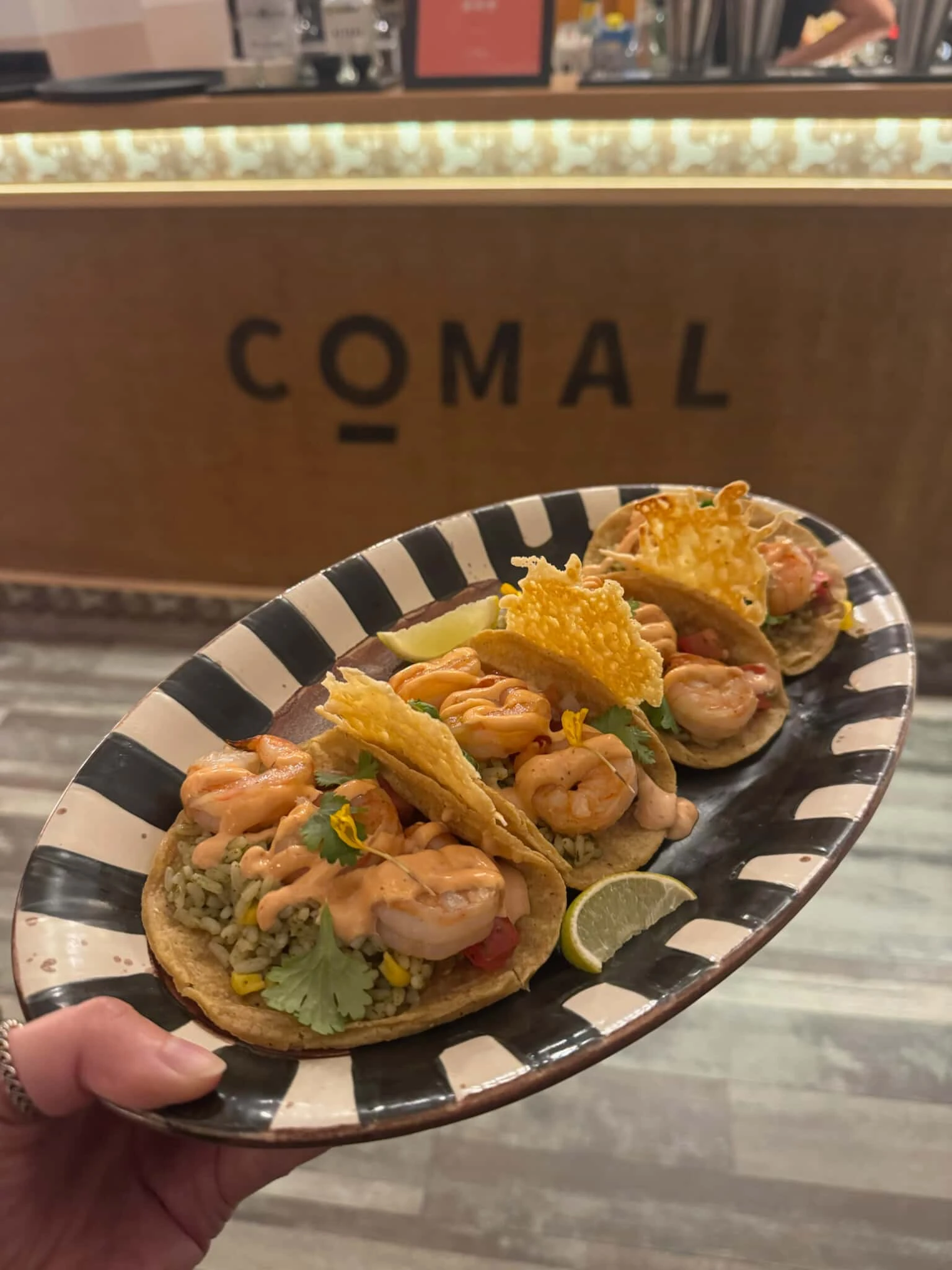 A plate of delicious shrimp tacos from COMAL, garnished with lime and served on a stylish black and white striped plate.