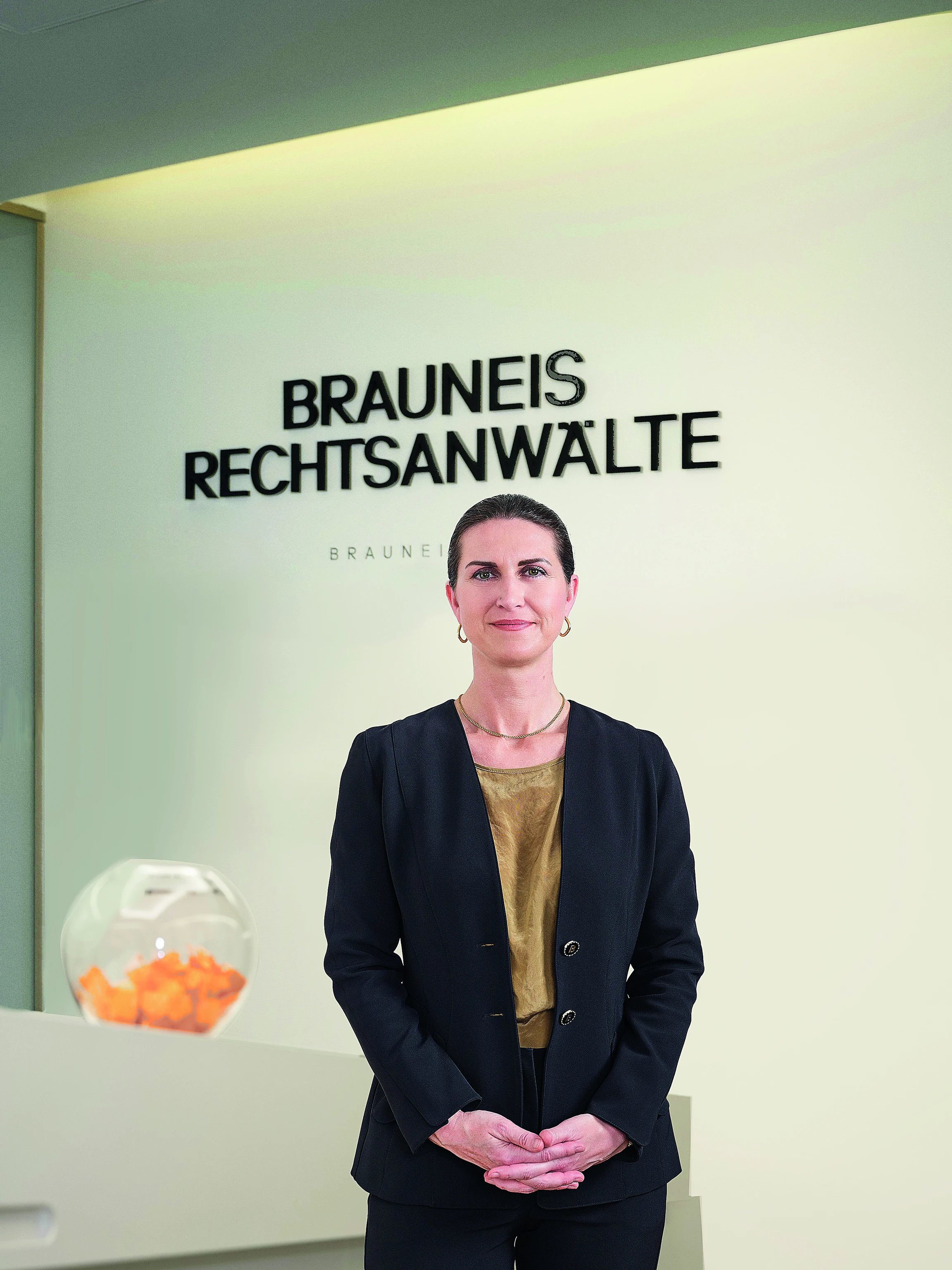 Linda Poppenwimmer vor einer weißen Wand mit der Aufschrift „Brauneis Rechtsanwälte"