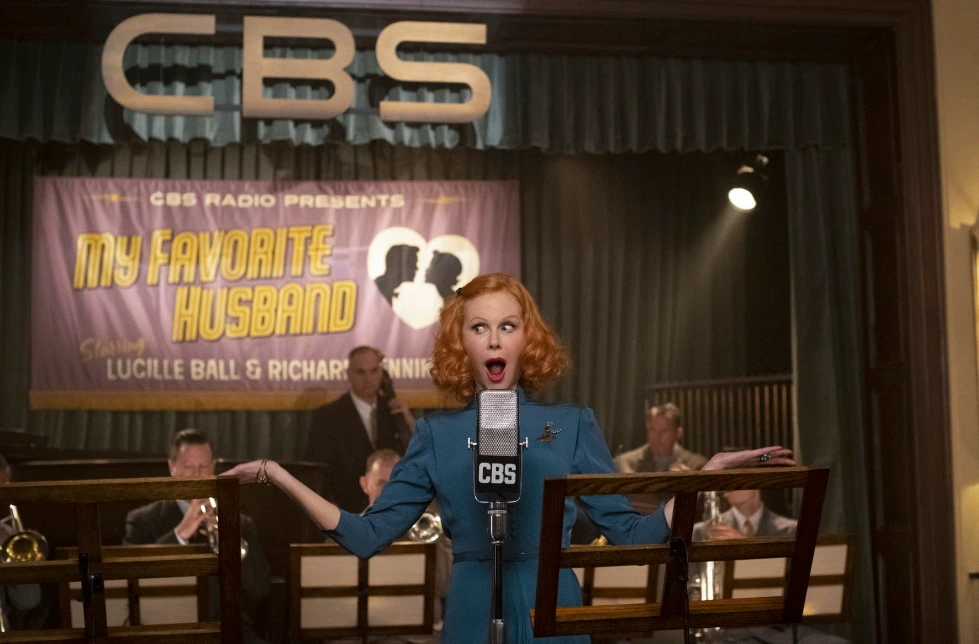 Nicole Kidman macht vor einem Mikrofon eine überraschte Geste, im Hintergrund sitzen Trompeter