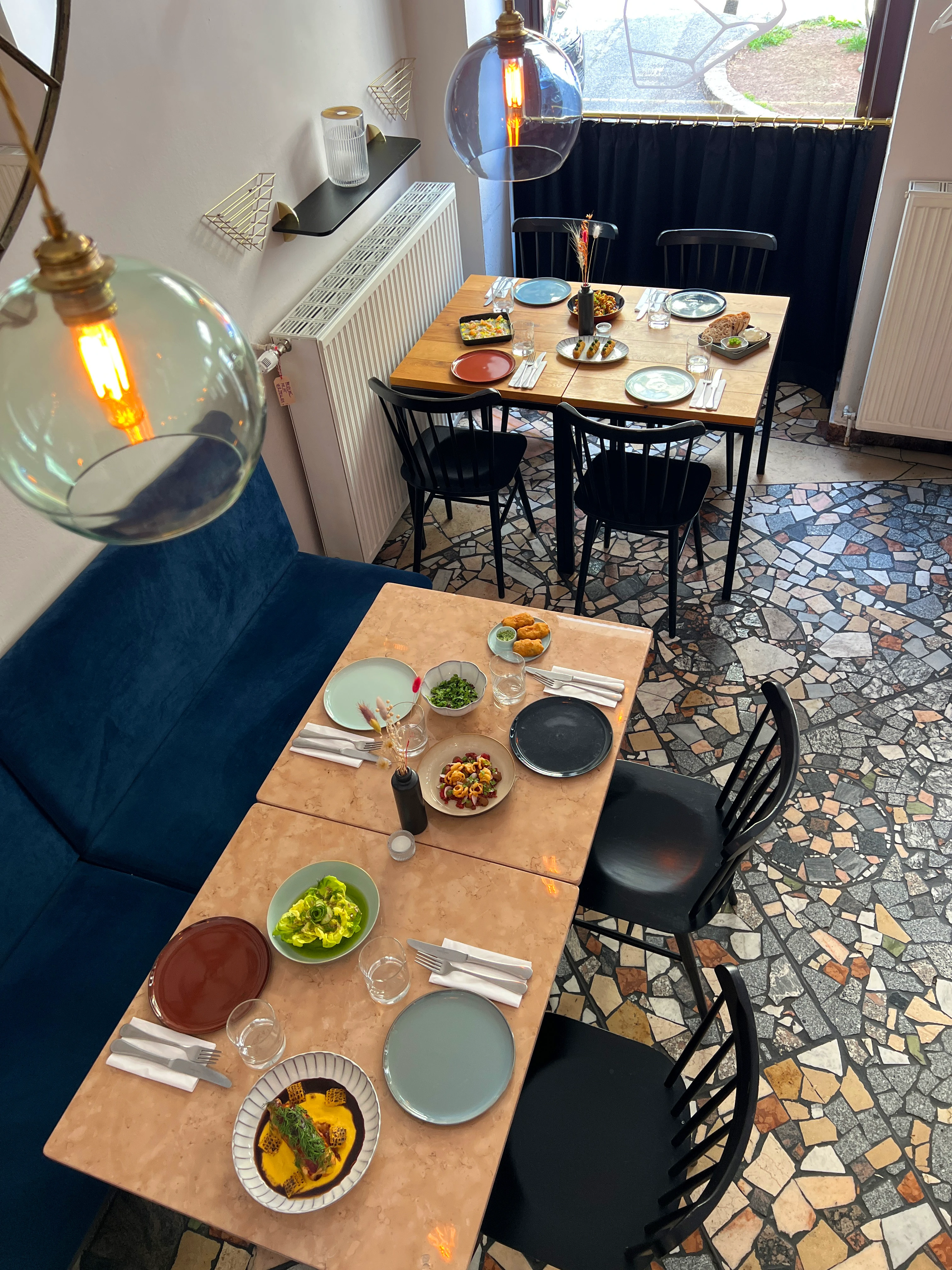 Restaurant setting with two tables set for dining, featuring various dishes and a mosaic tile floor.
