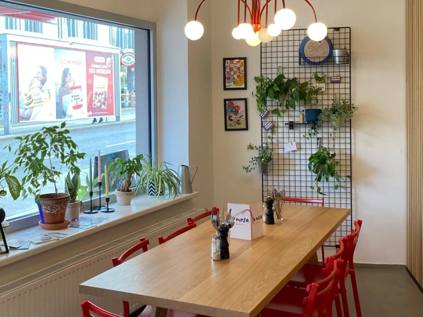 Restaurant Interieur mit Holztisch, roten Stühlen, Fensterblick und Pflanzen