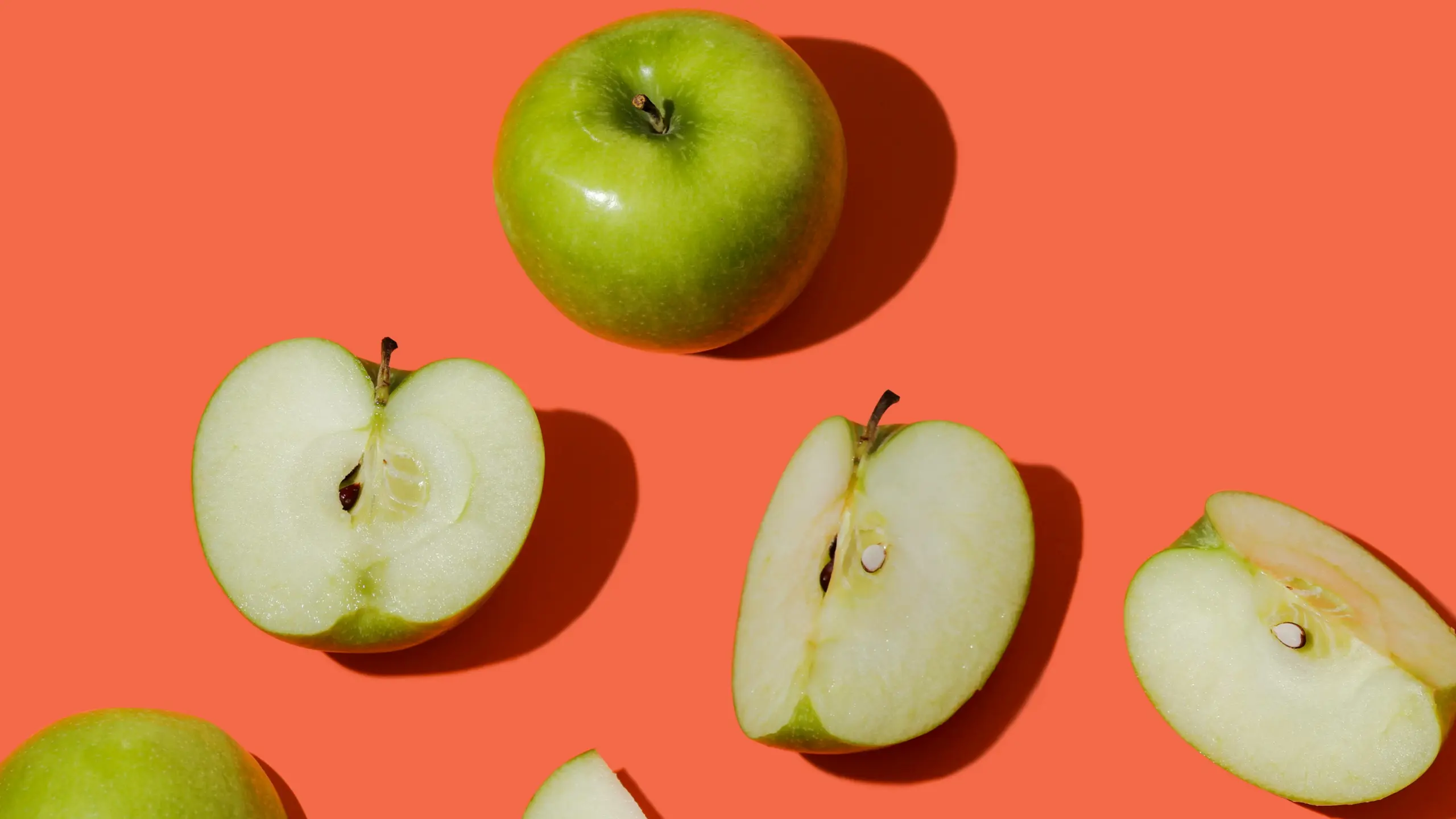 Mehrere Äpfel (als ganzes und geschnitten) vor Orangem Hintergrund